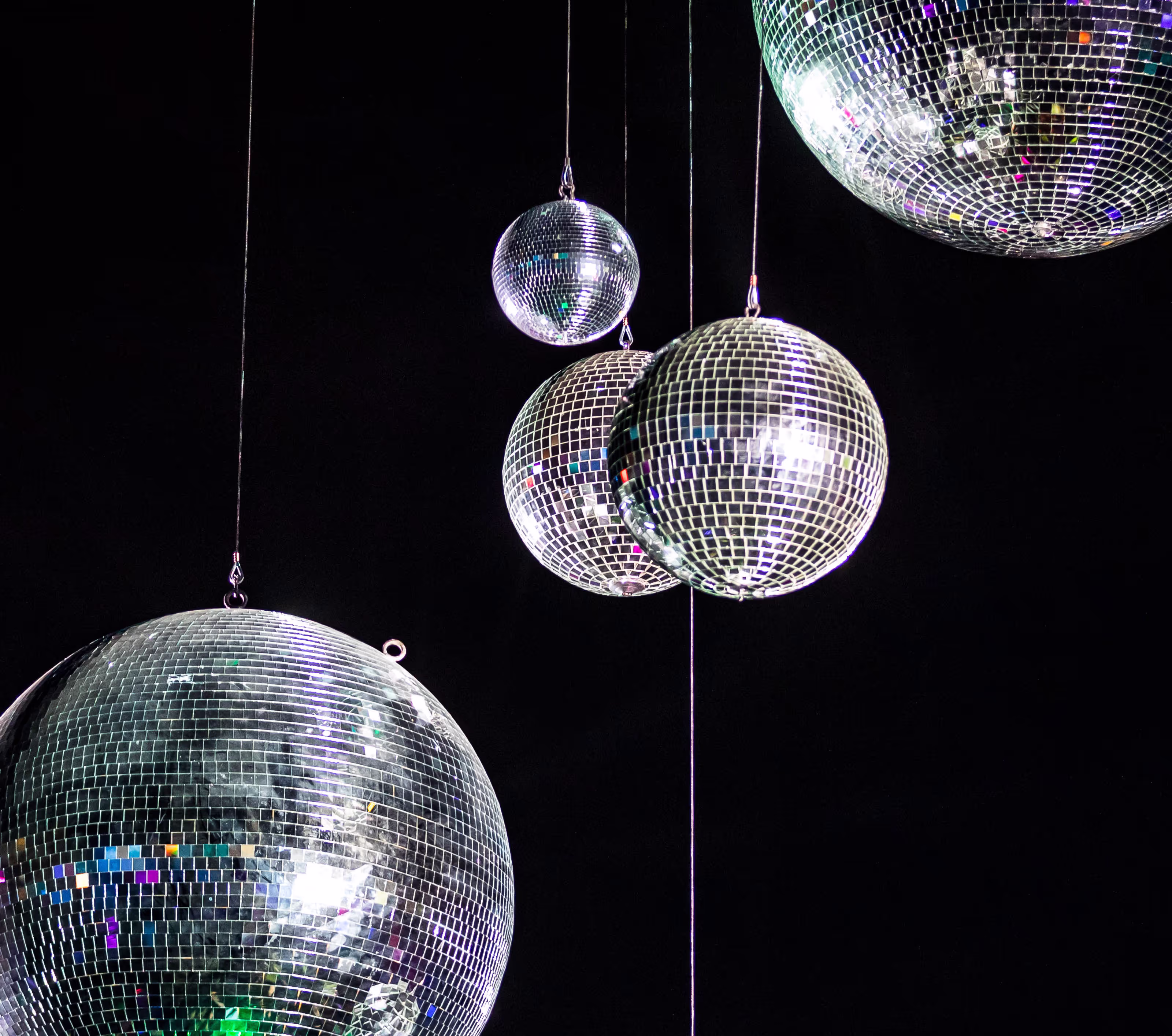 Four mirrored disco balls of varying sizes hanging against a black background.