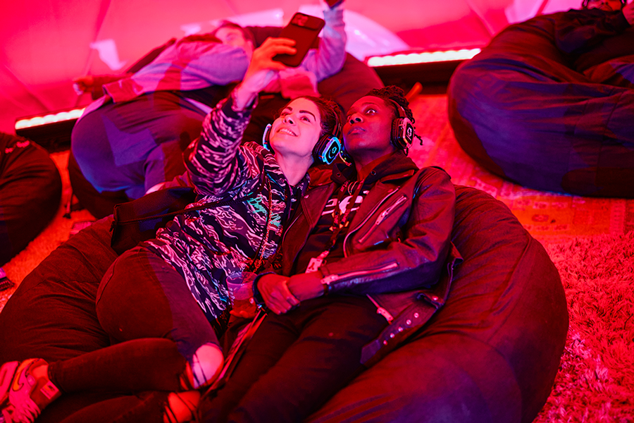 Two guests in headphones reclining on beanbags in the red-lit Soundbath dome