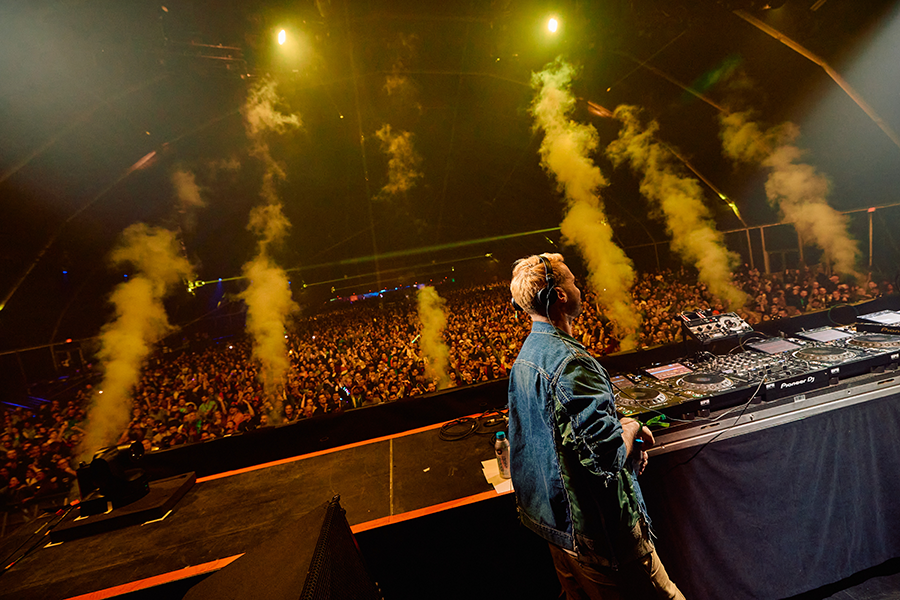 A dj in front of a large crowd at a concert.