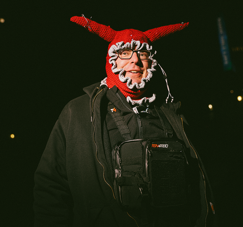 A man wearing a red devil mask and a camera.