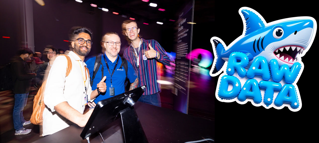 Three men posing with smiles and thumbs up at an event, with a colorful cartoon shark labeled RAW DATA on the right