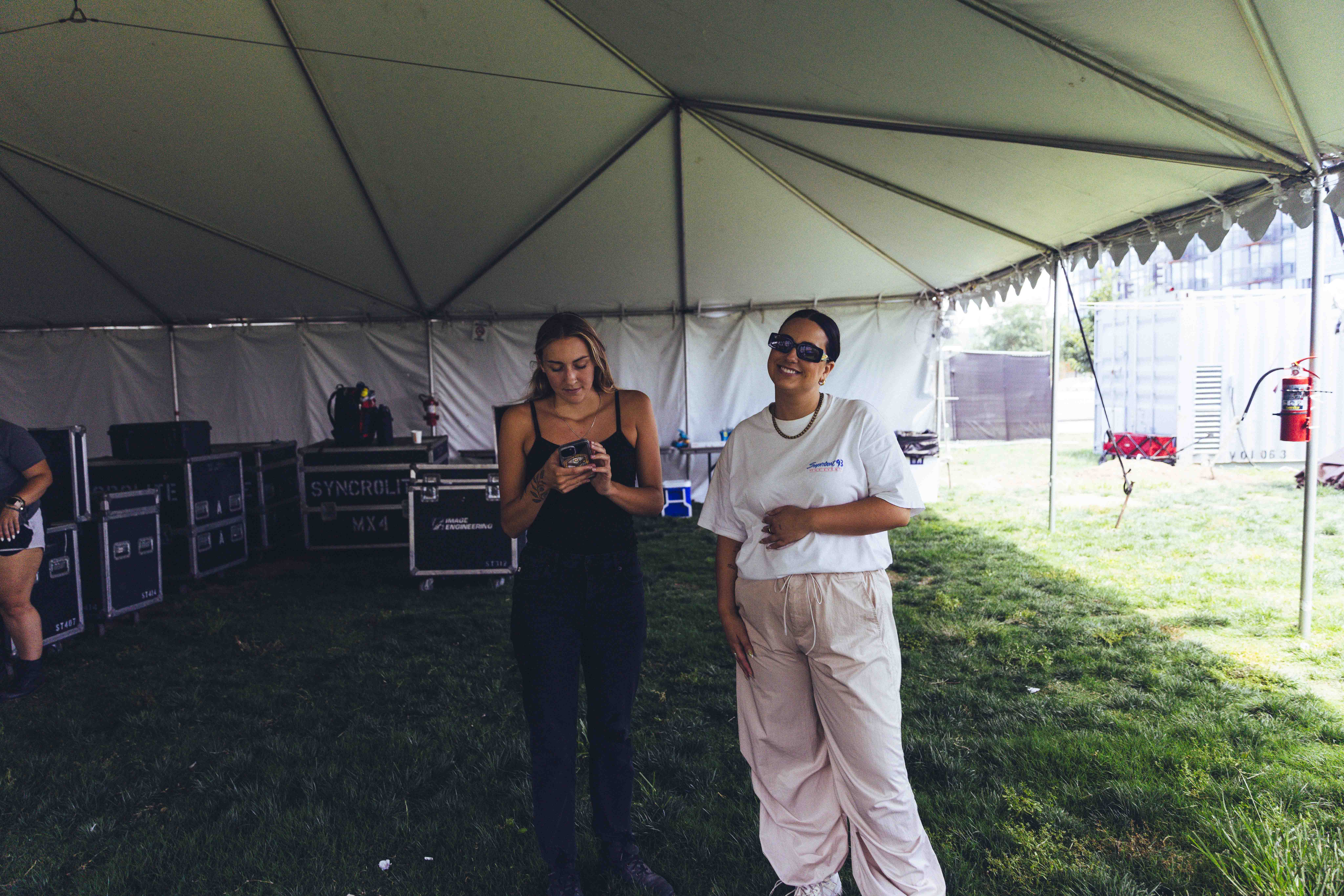 two people standing inside of an outdoor tent while one person looks at their phone