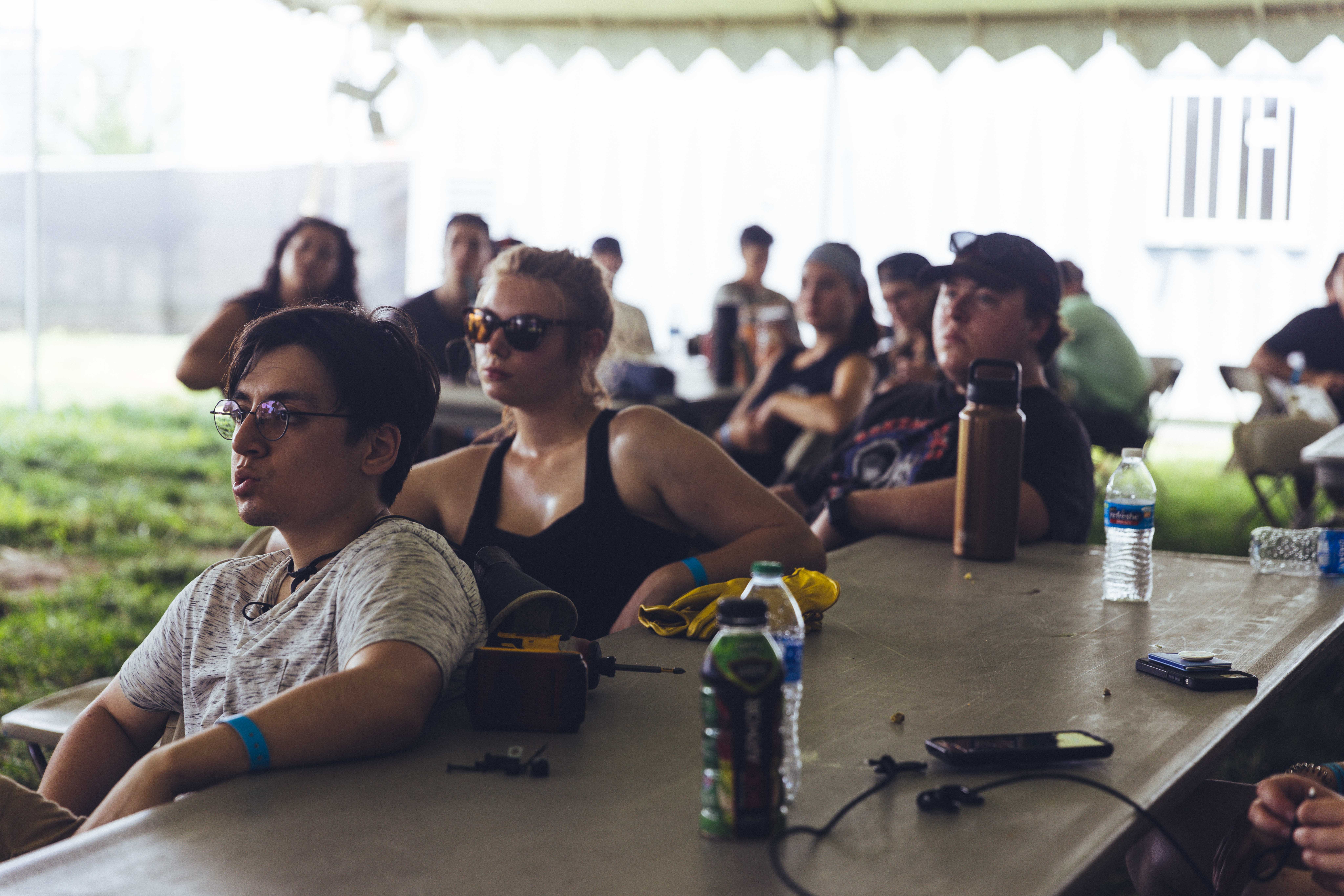 people sitting at a table outside listening to a speaker