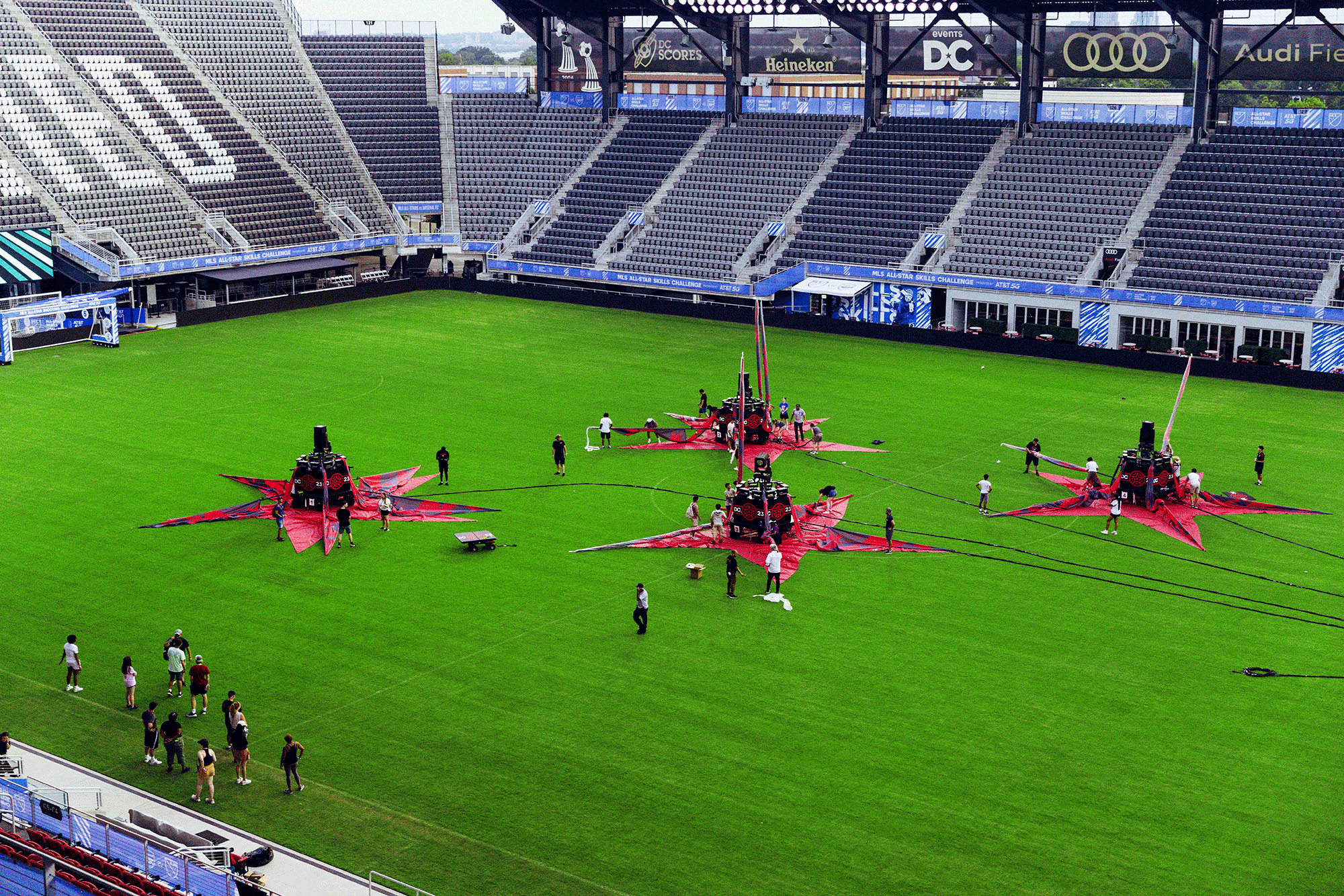 People assembling large red star-shaped structures on the field inside an empty soccer stadium with visible stands and advertisements.