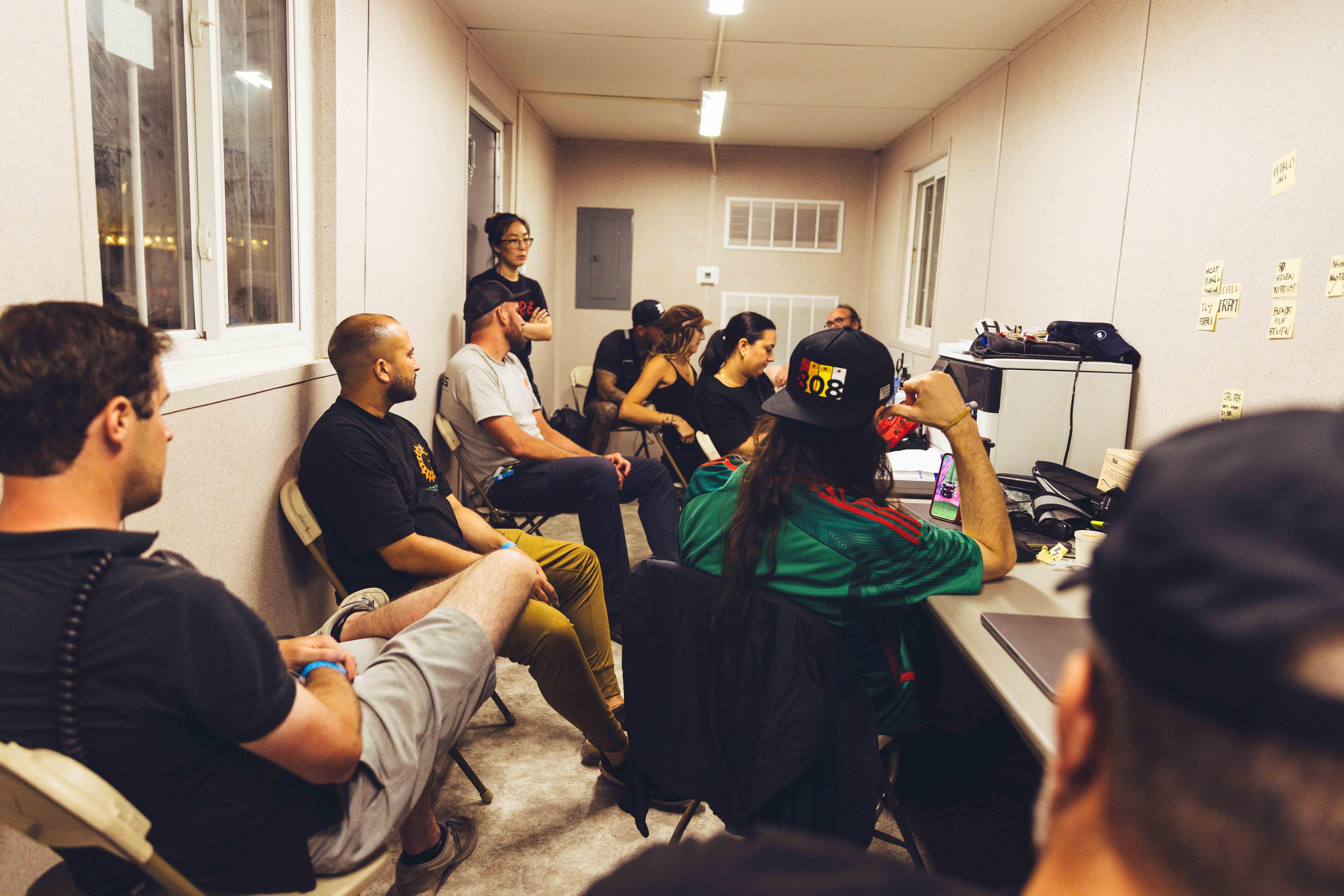 a lot of people crammed in a small beige room looking at computers