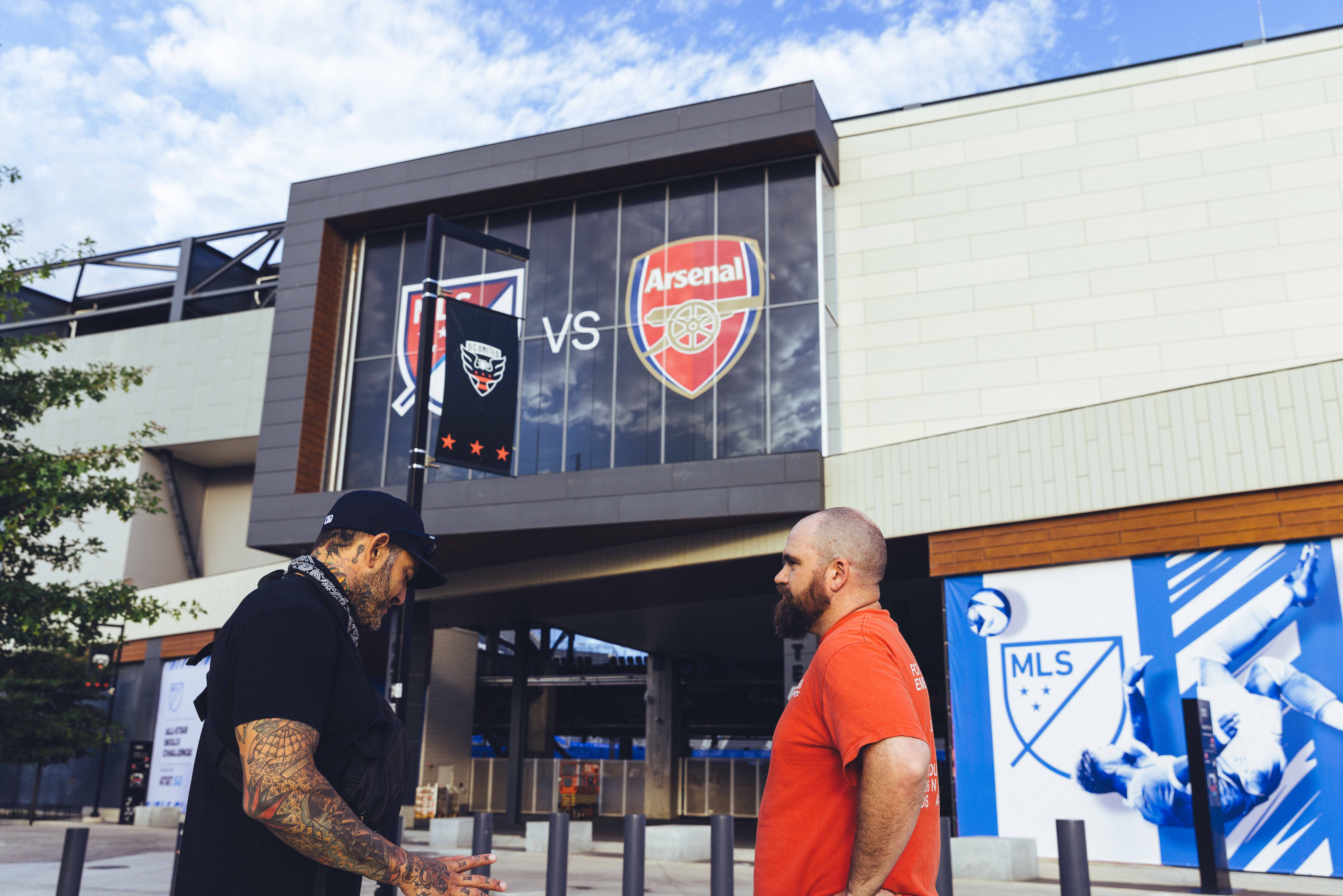 two people speaking to each other outside in front of a large building