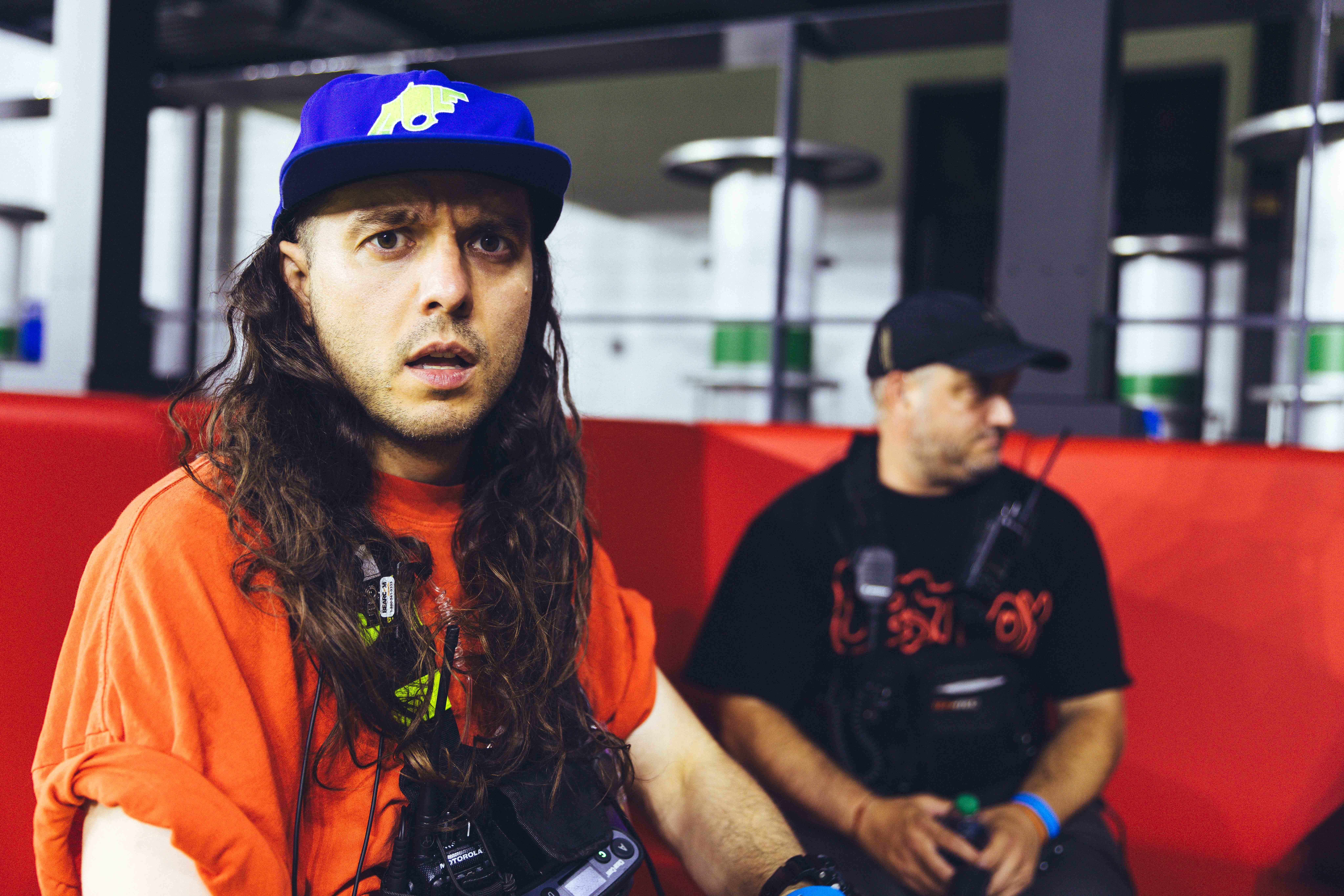 two men with hats face the camera with a red wall in the background