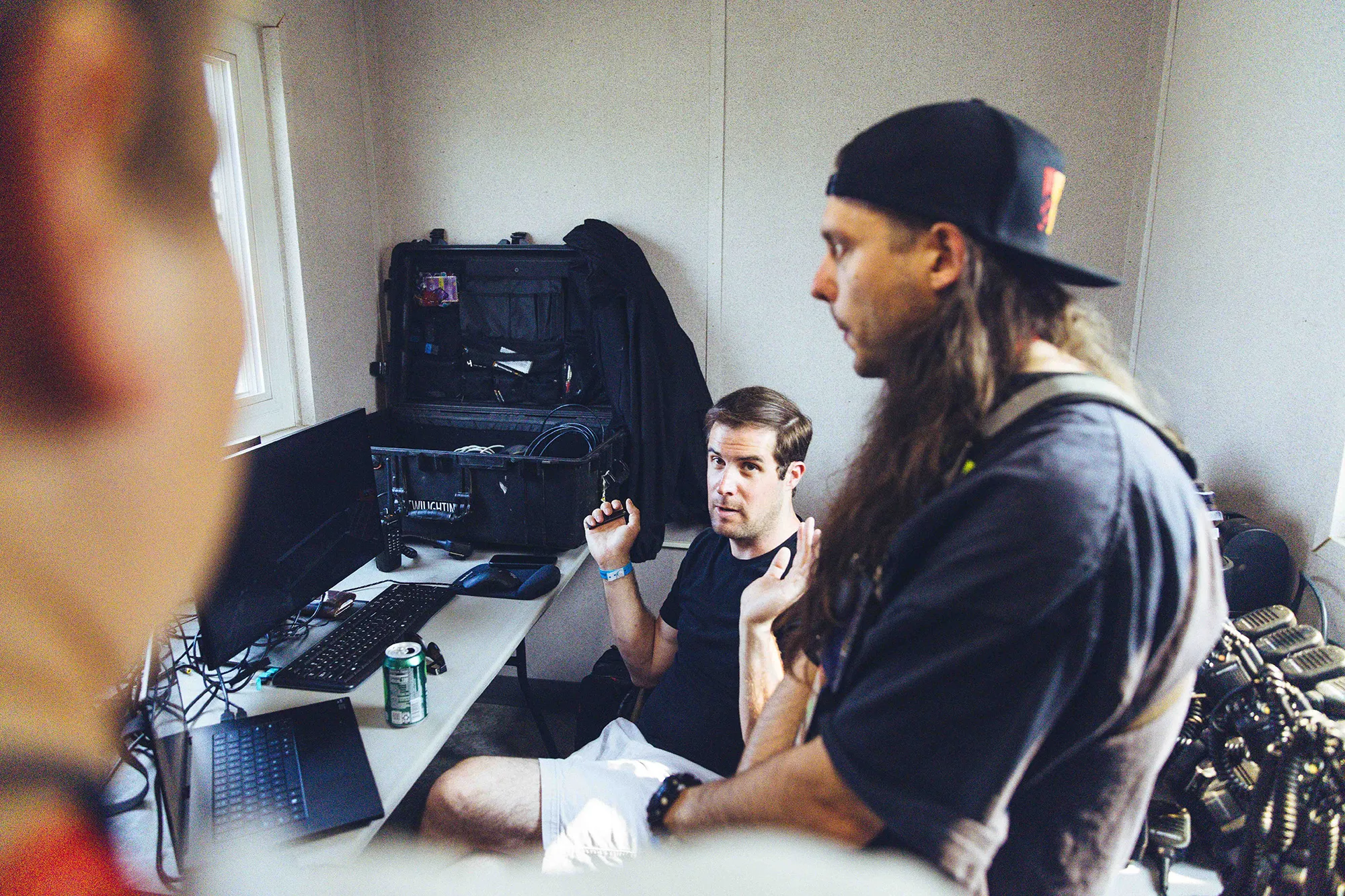 two men in a room dressed in black looking at computer monitors