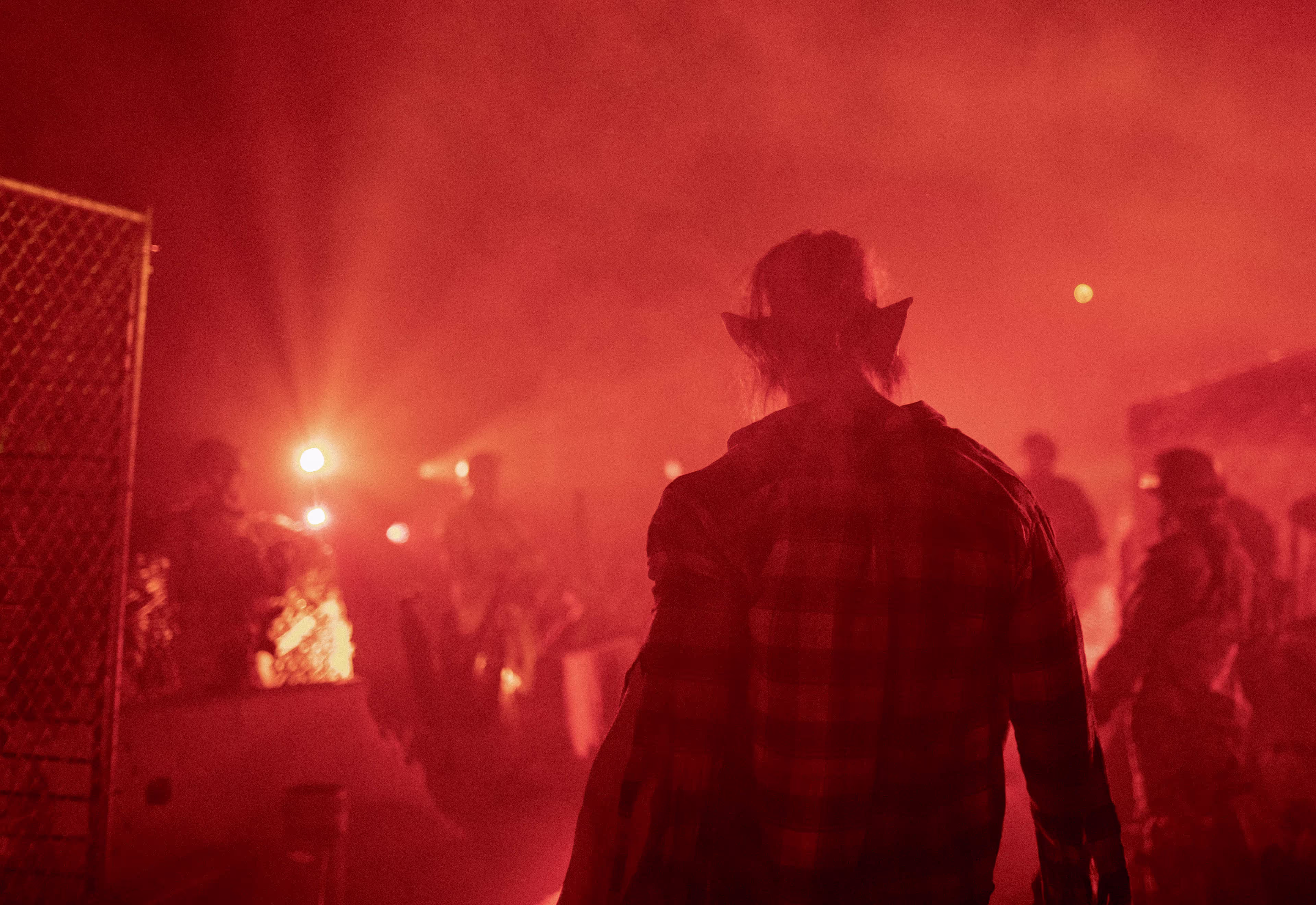 Person with pointed elf ears in a checkered shirt standing in a red-lit foggy outdoor area.