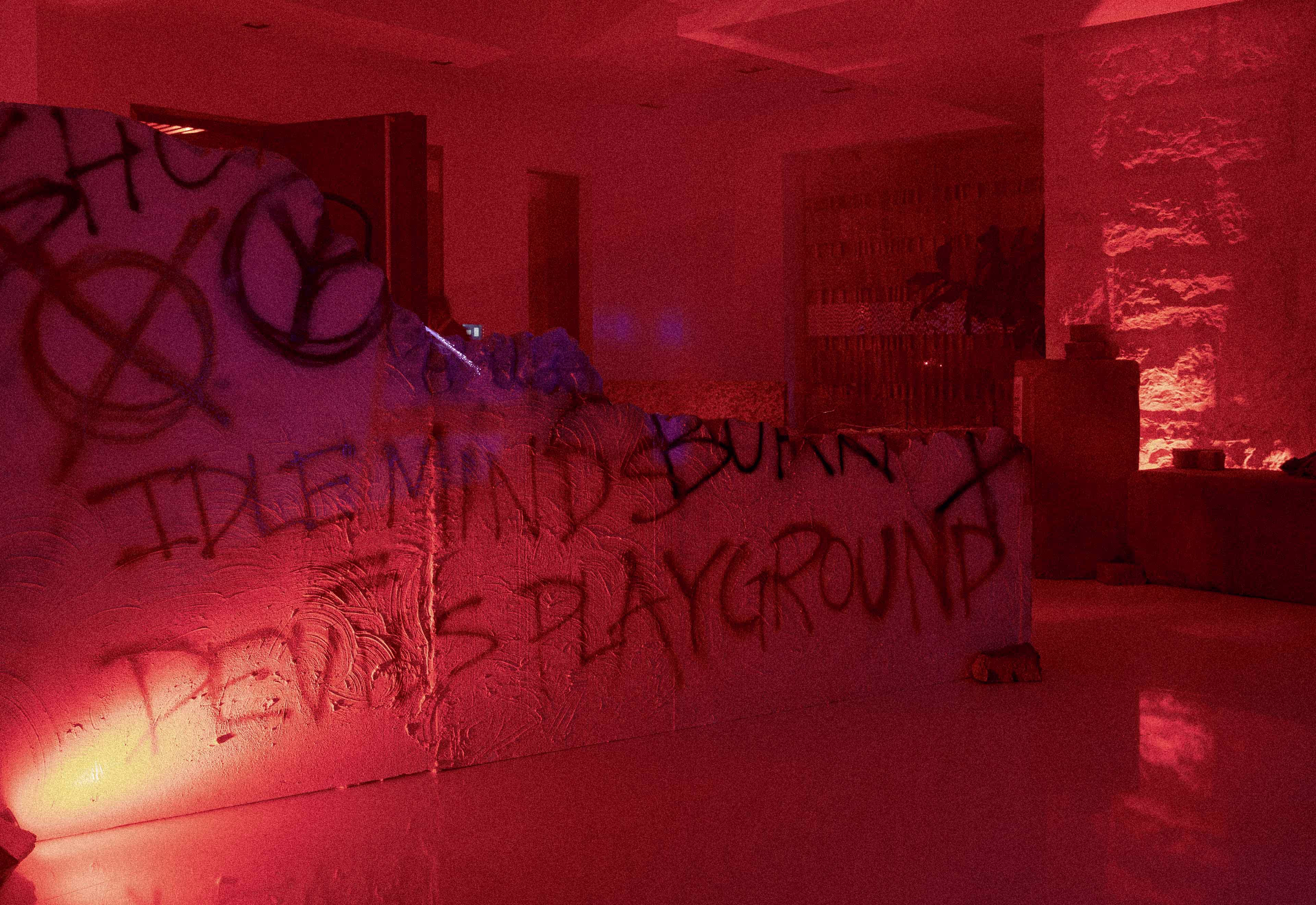 Dimly lit indoor scene with graffiti on a textured wall under red lighting.