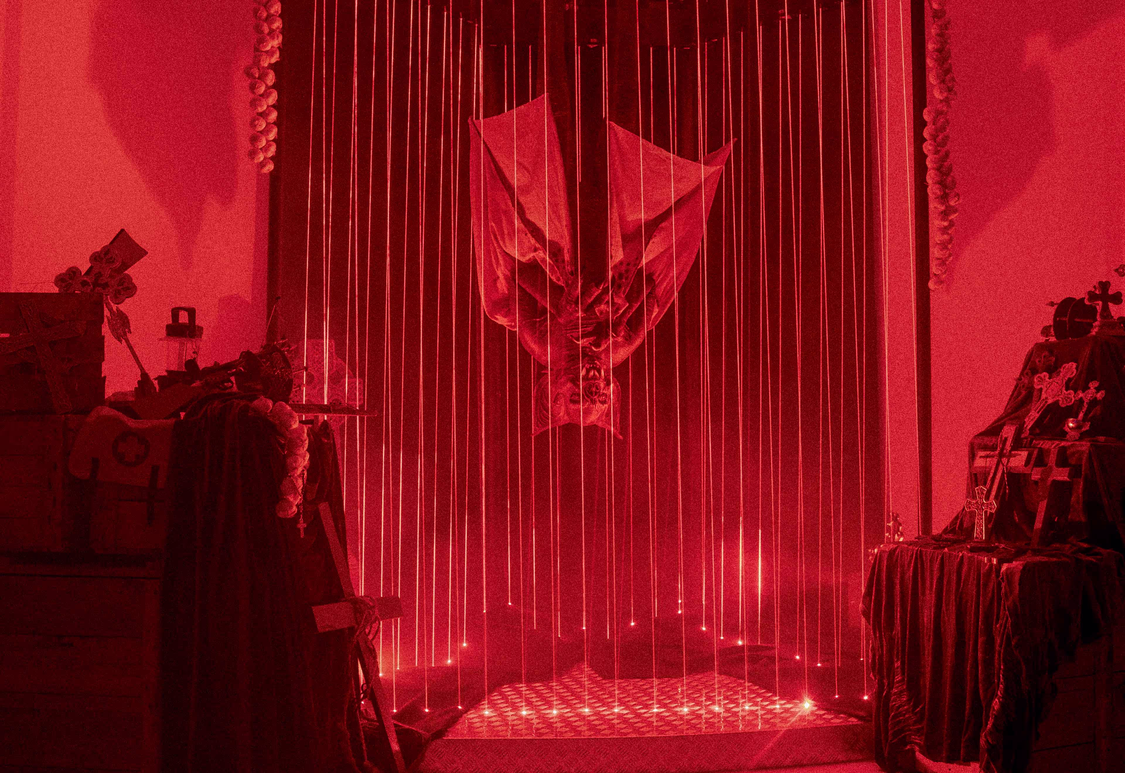Dimly lit red room with an upside-down bat figure suspended behind vertical light beams.