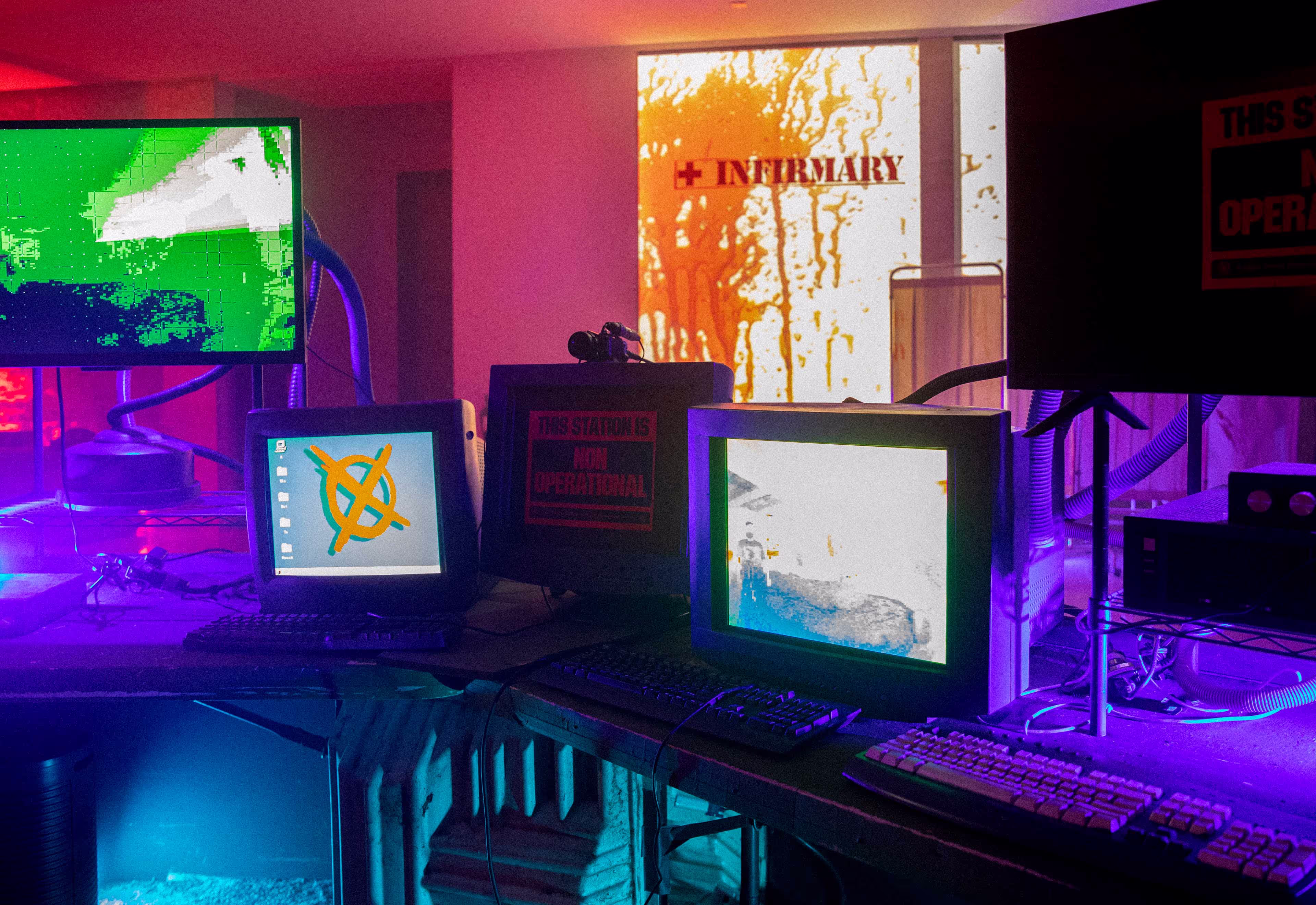 Dimly lit room with multiple old computer monitors and a wall sign reading 'INFIRMARY'.