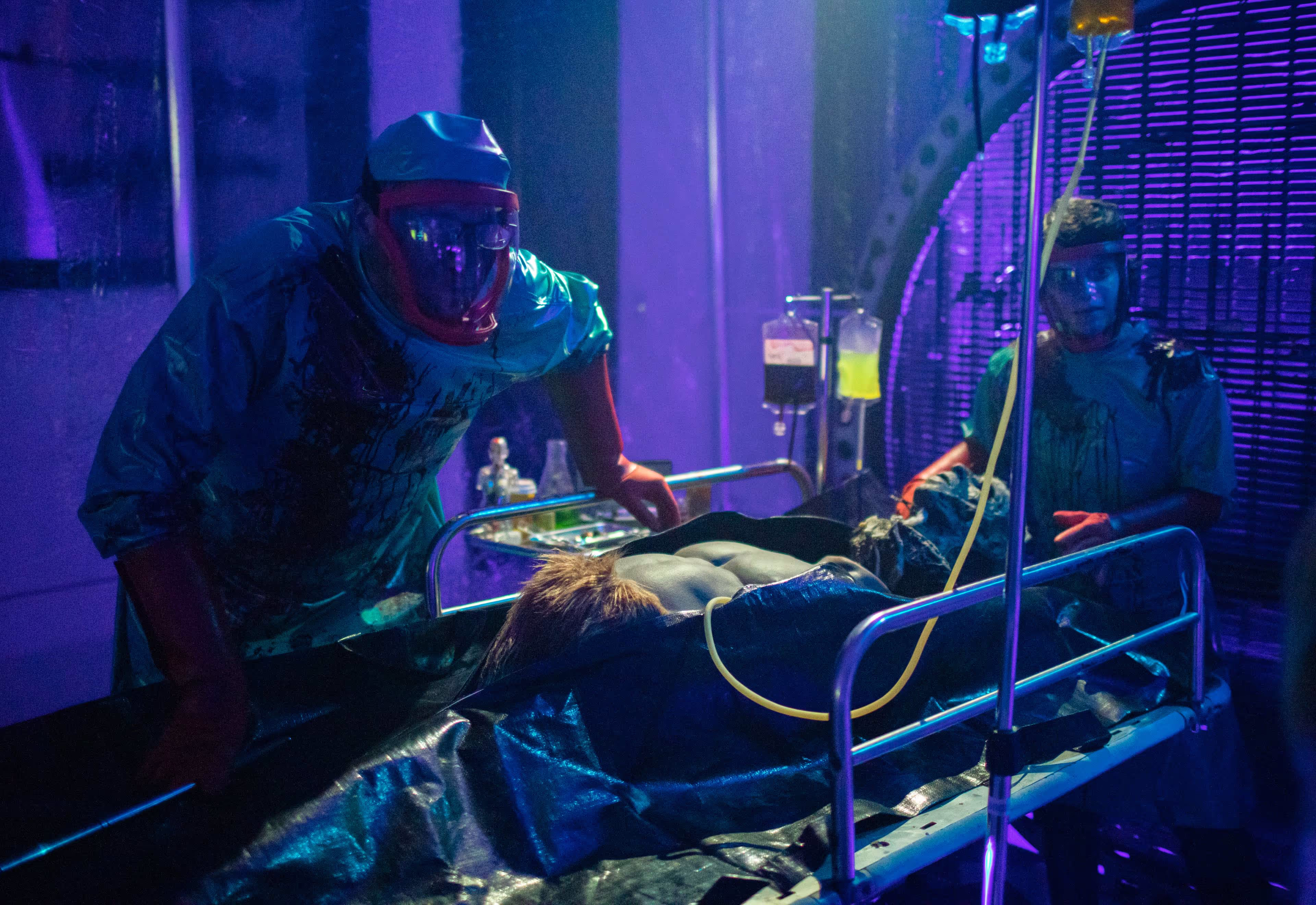 Two people in protective suits and face shields attending to a body on a hospital gurney.