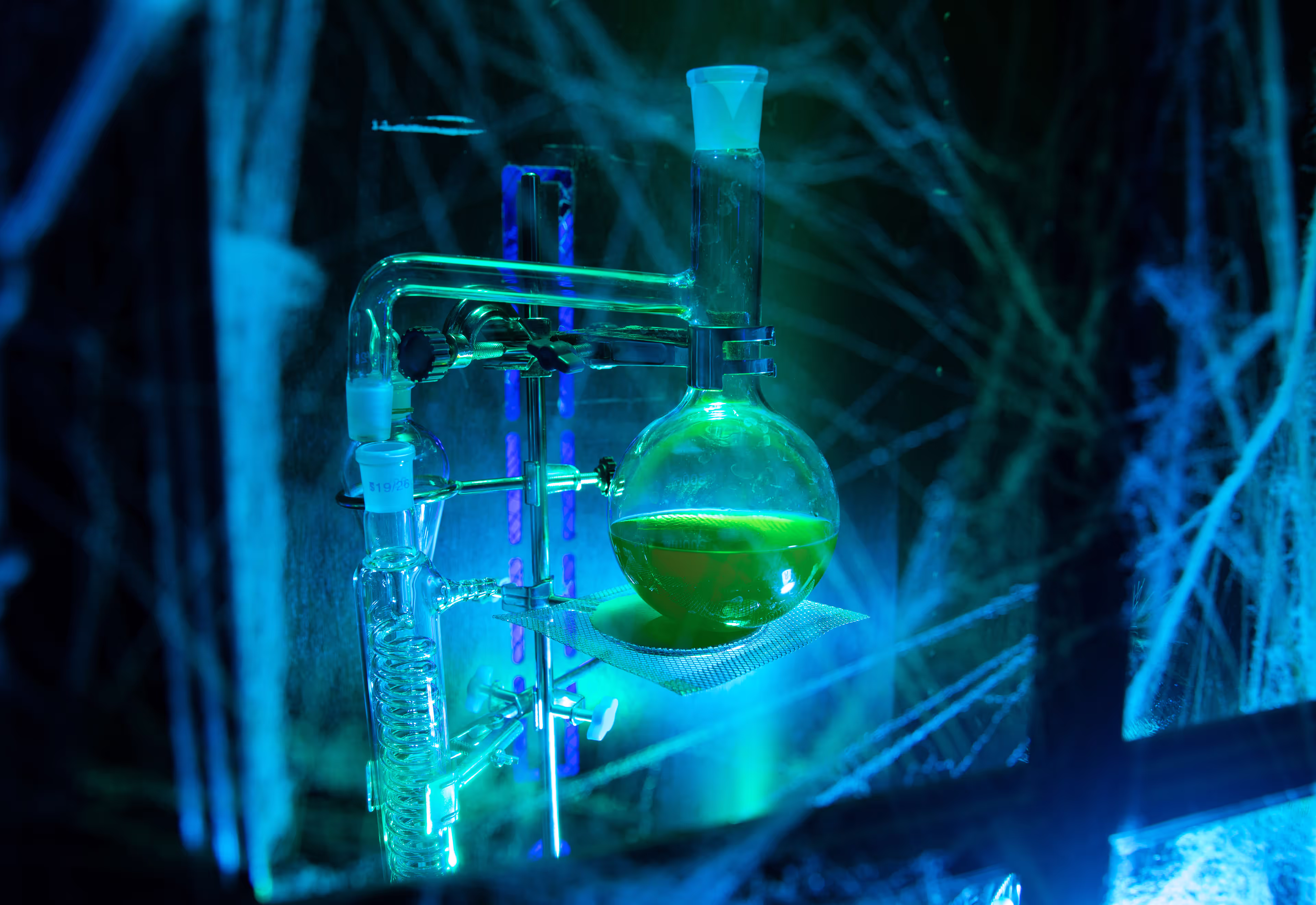 Laboratory glass distillation apparatus with round-bottom flask containing green liquid.