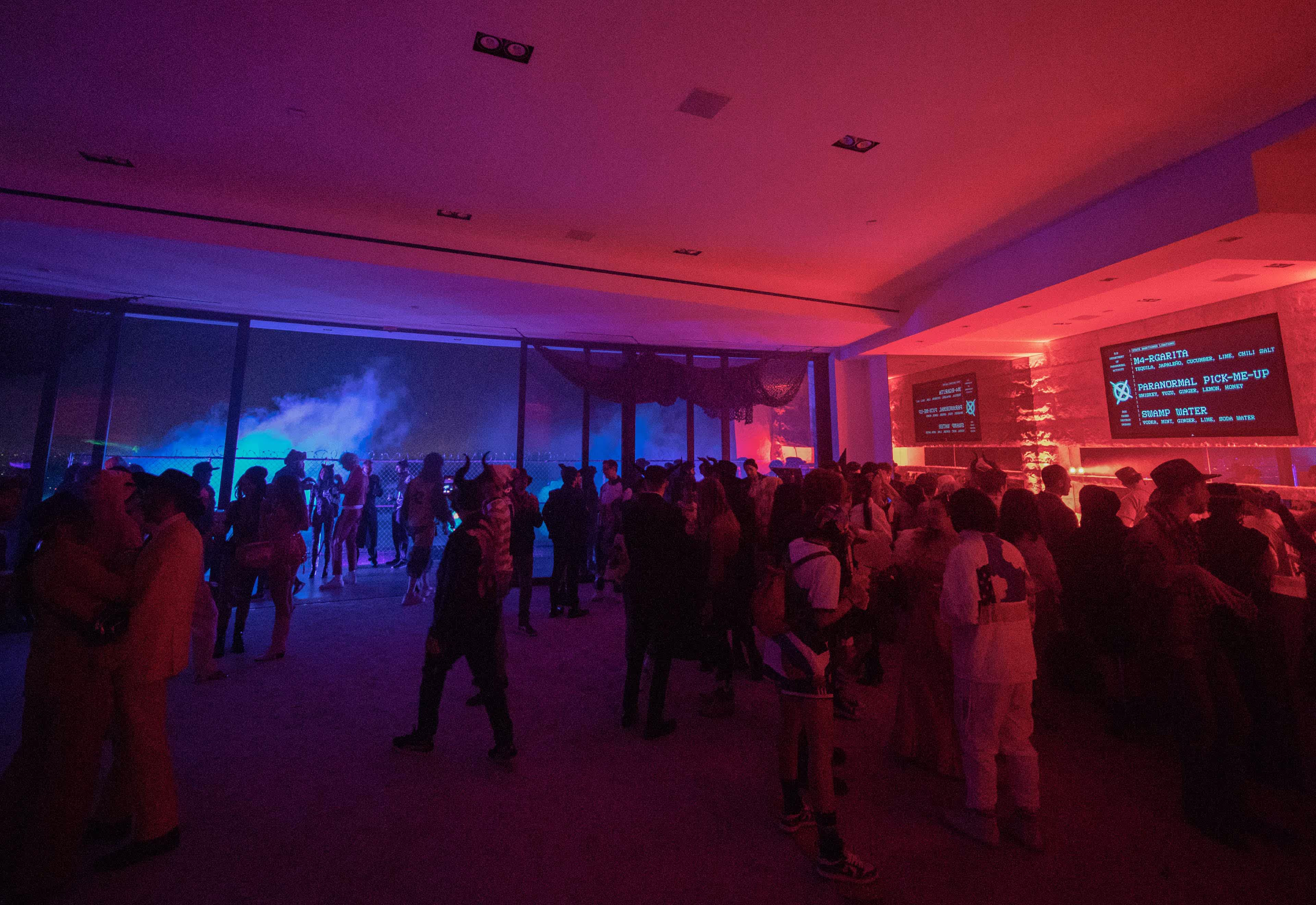 Crowd of people socializing indoors under red and blue lighting.