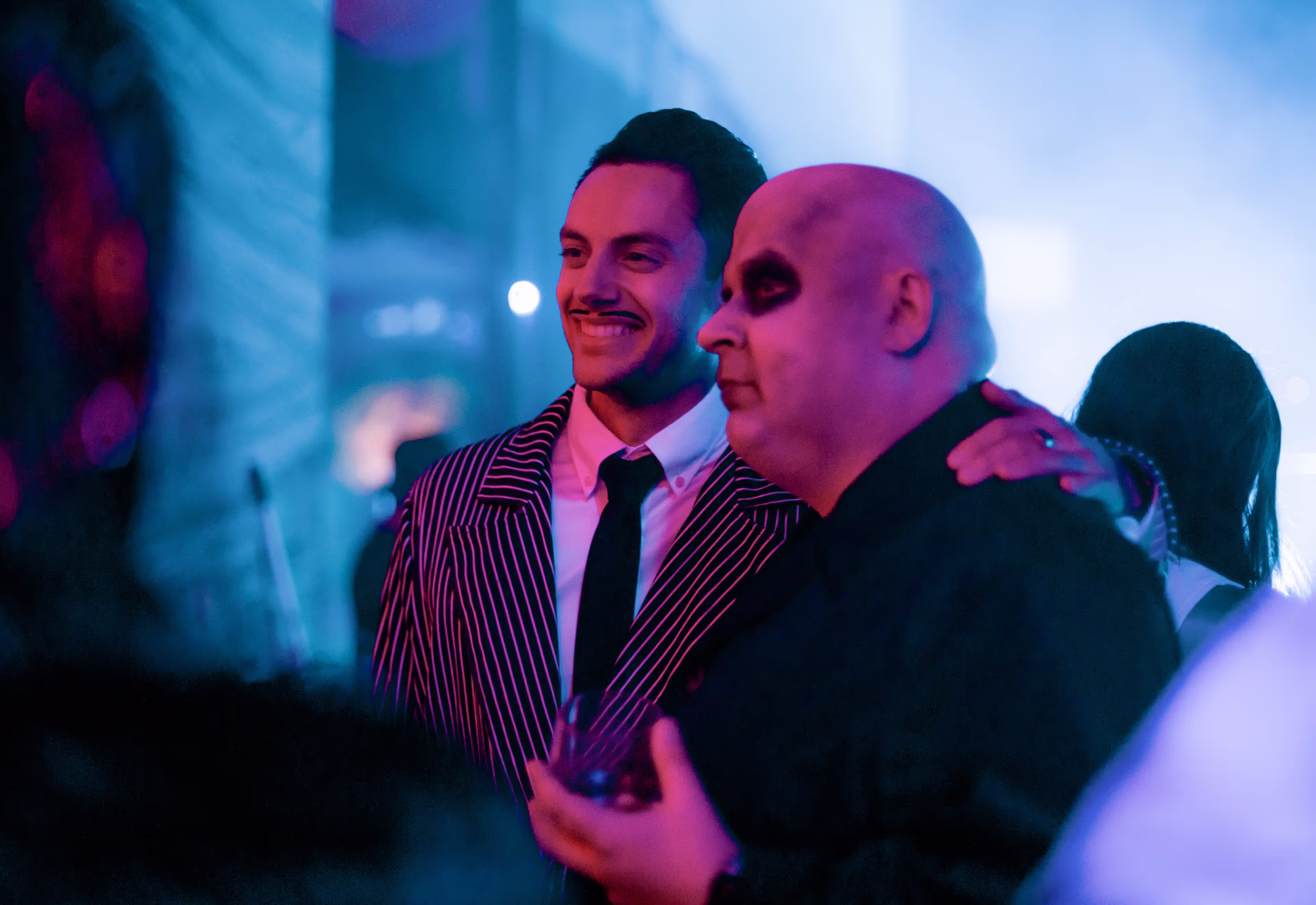 Two men at a party, one in a striped suit and tie smiling.