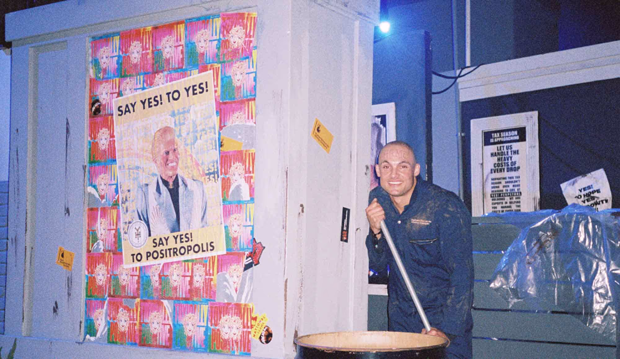 A man standing in front of a poster holding a plunger.