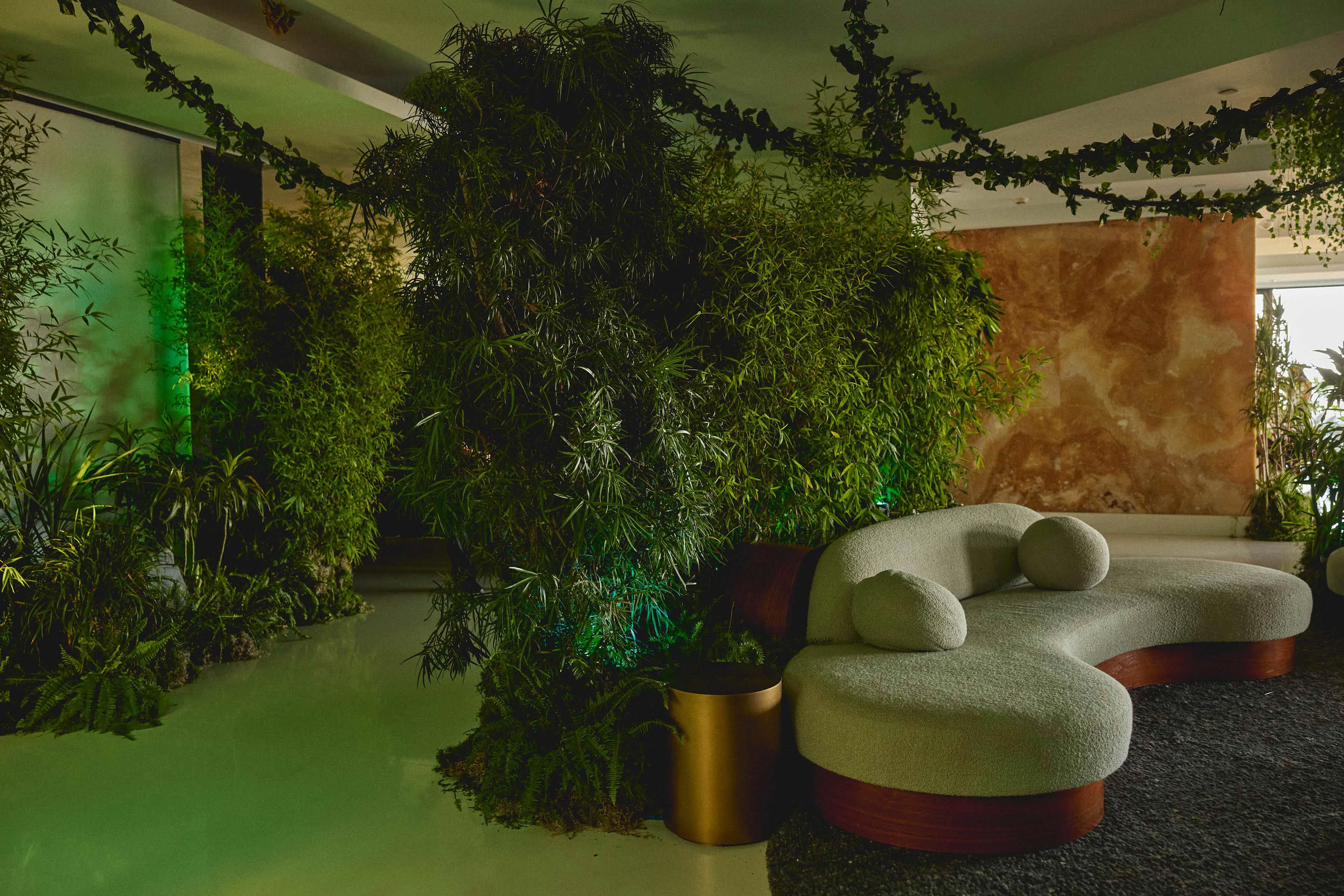 Curved modern sofa with round cushions surrounded by lush green plants and hanging vines in a stylish, earthy indoor space.