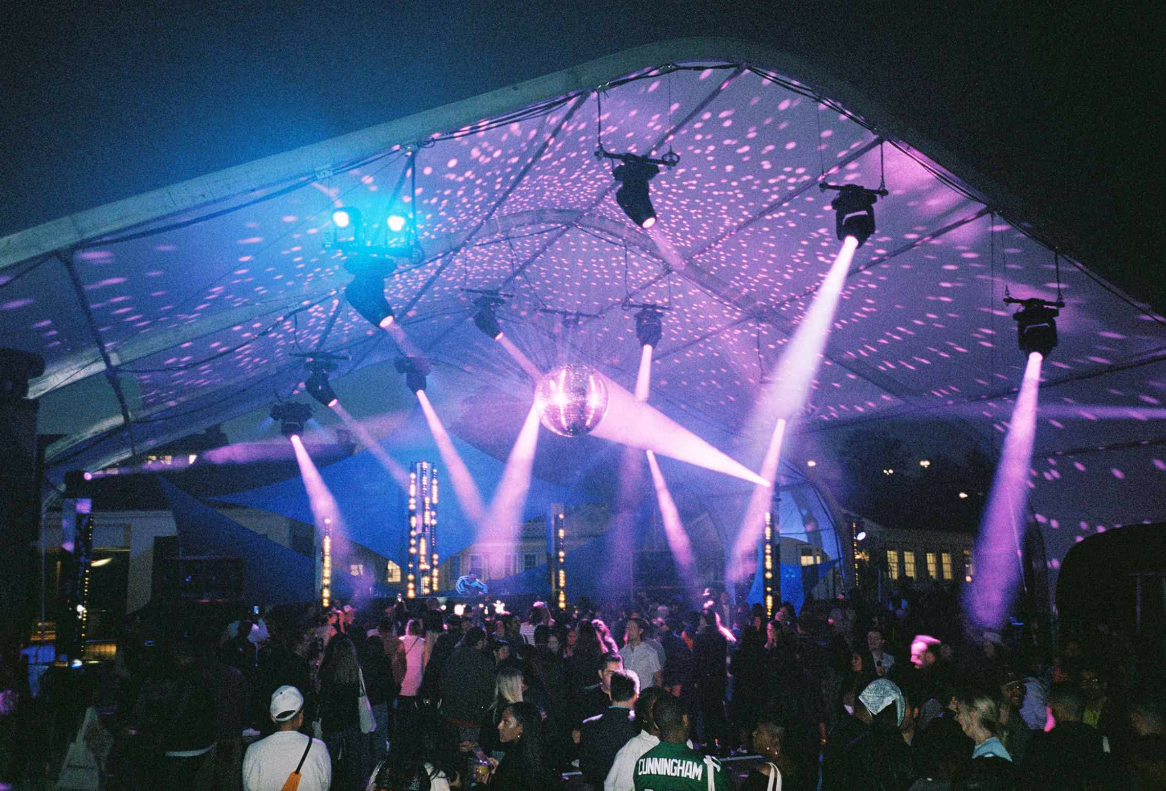 A crowd of people standing under a tent at night.