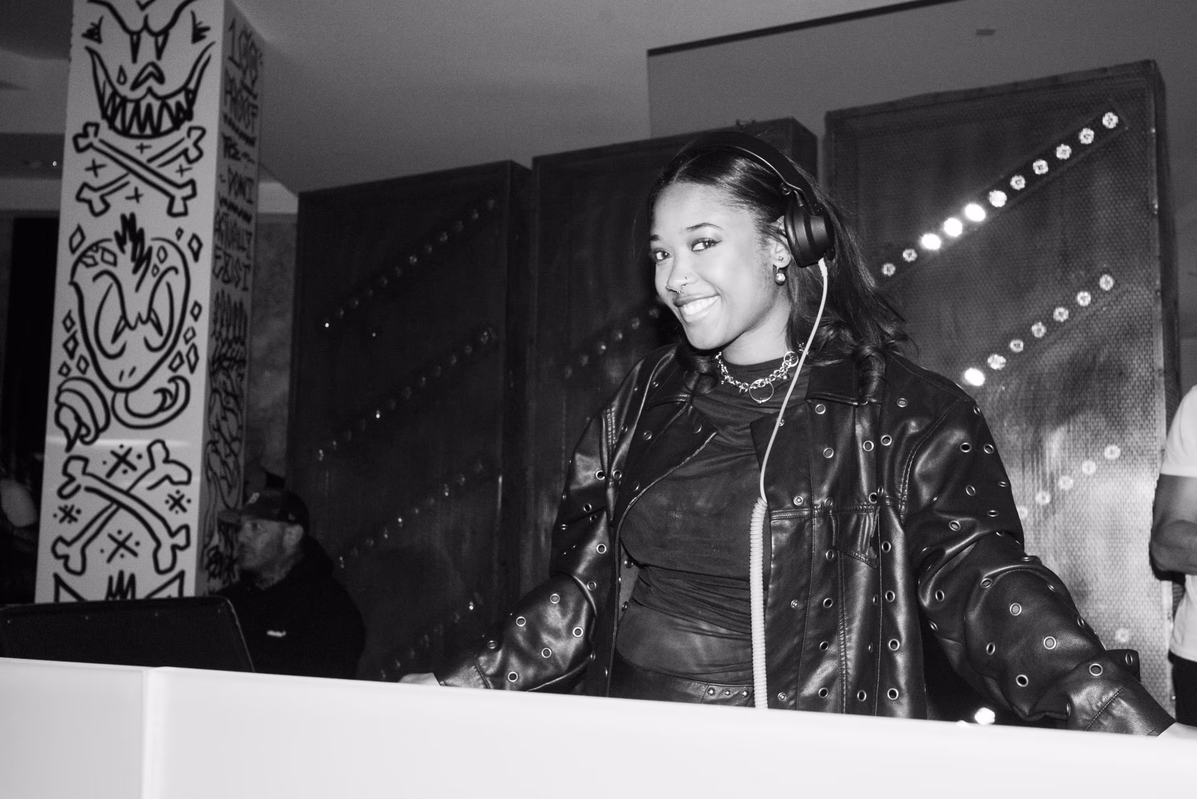 A woman wearing headphones standing in front of a wall.