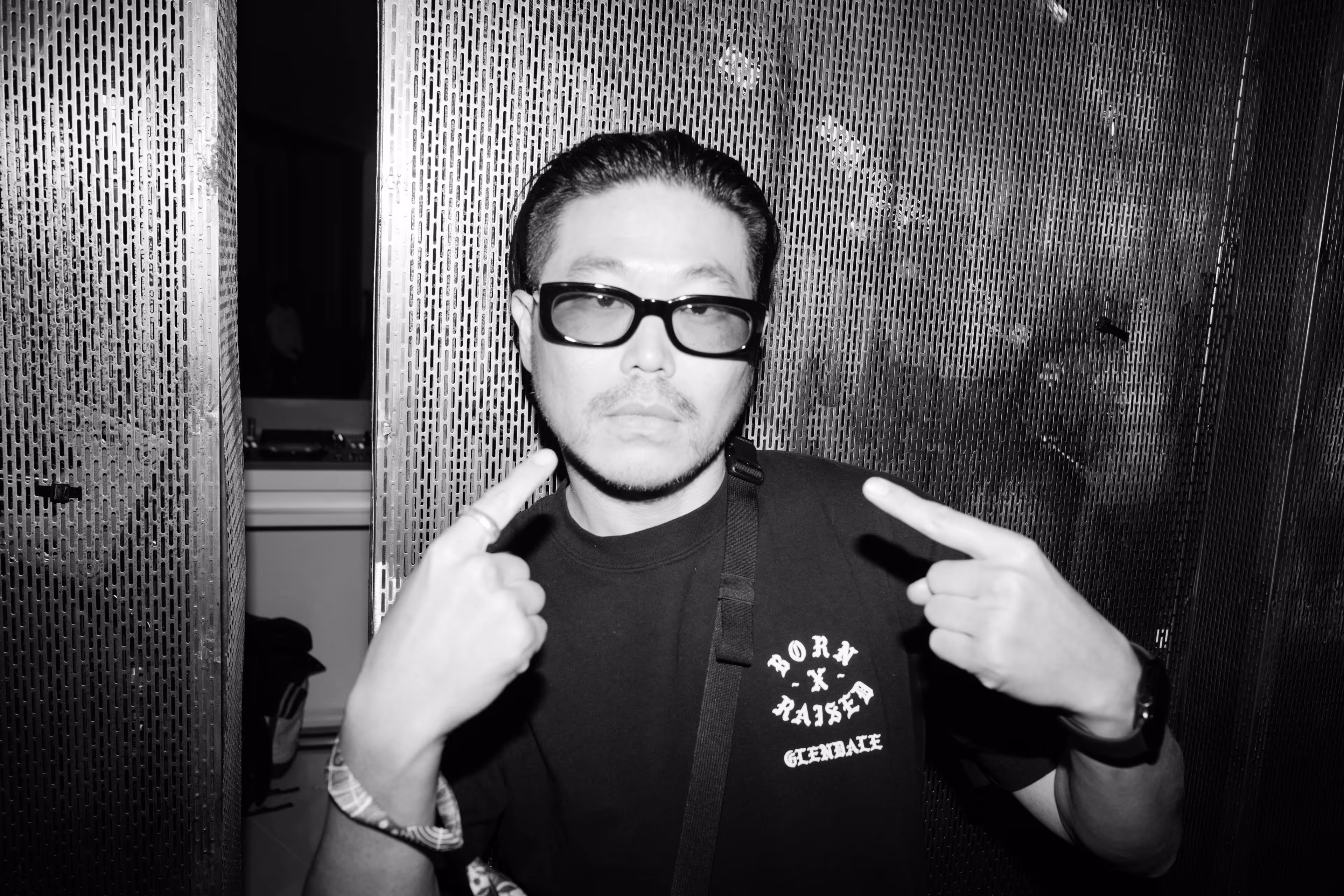 A man in a black shirt and glasses pointing at the camera.