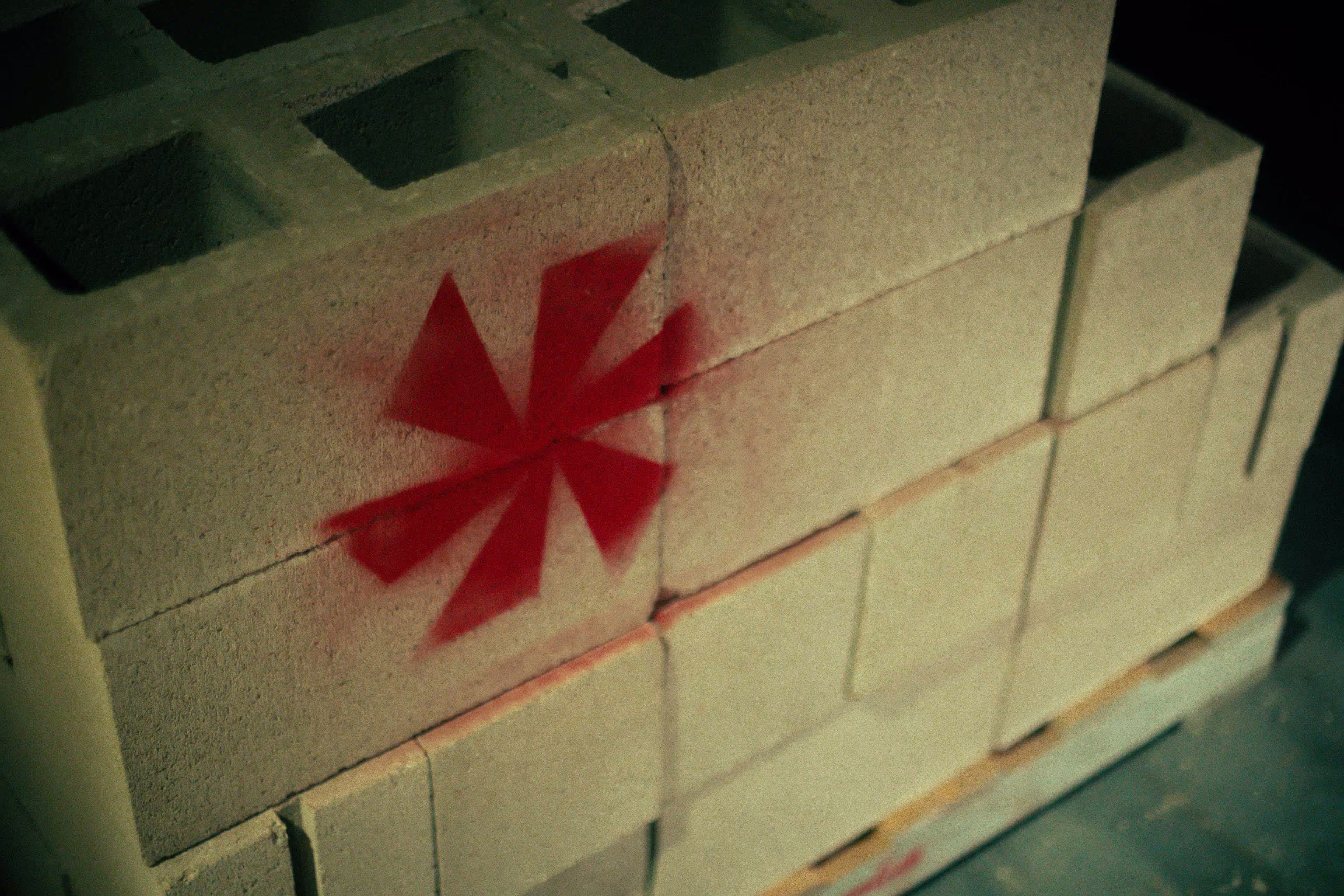 Stack of cinder blocks with one block spray-painted with a red eight-pointed star-like symbol.