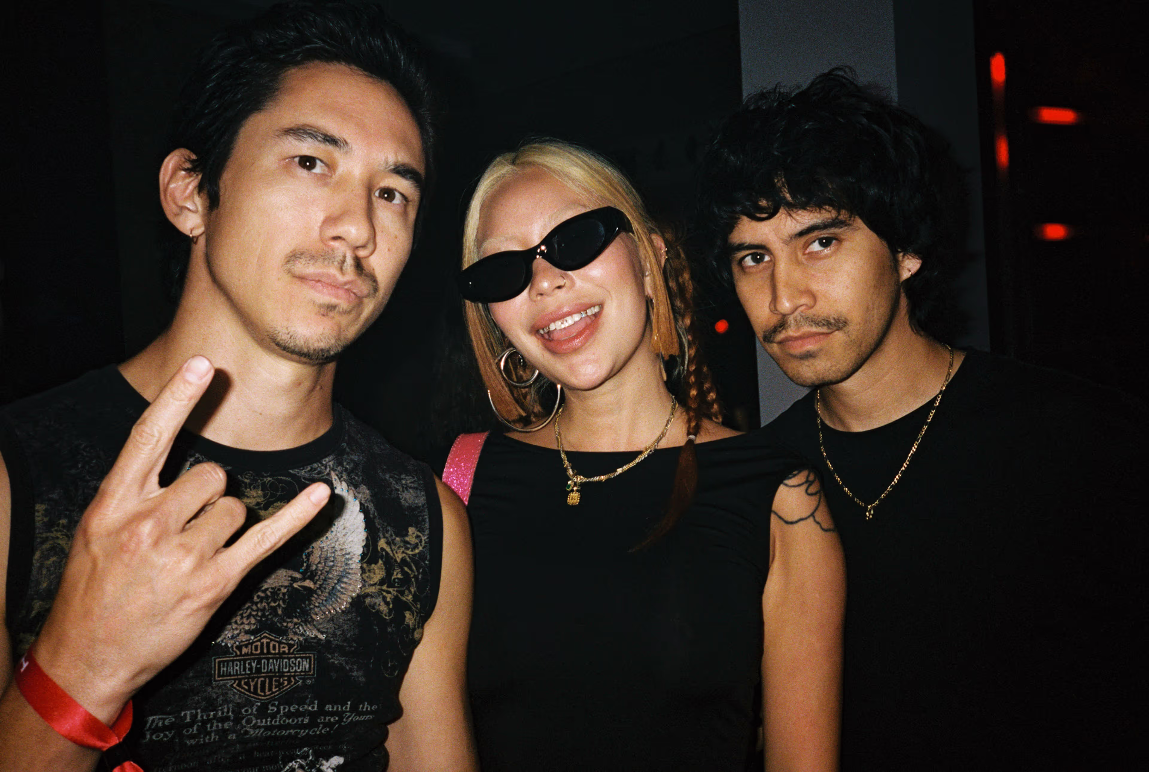 Three young adults posing together in a dimly lit setting.