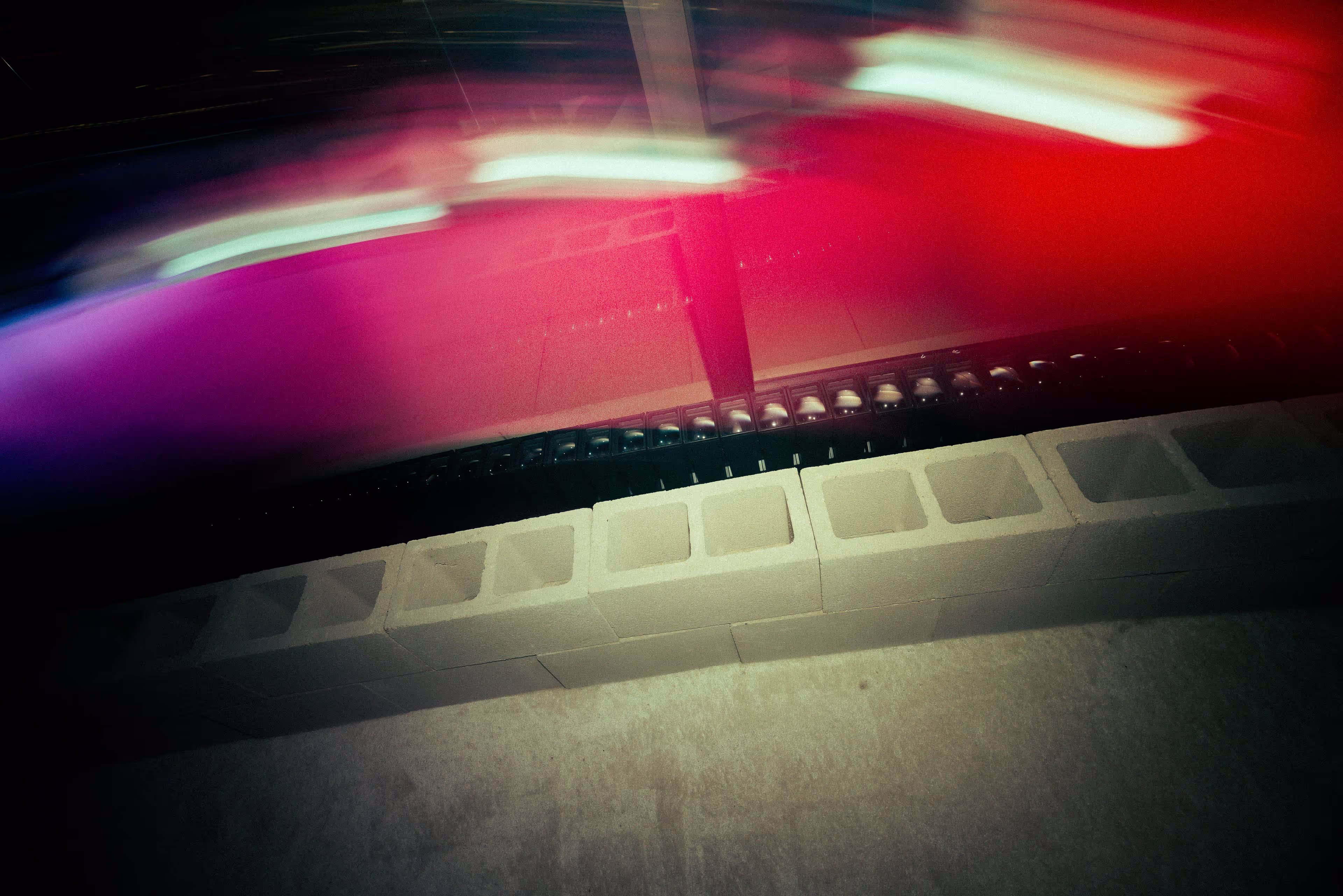 Blurred red, purple, and white streaks above a row of concrete cinder blocks on a concrete floor.