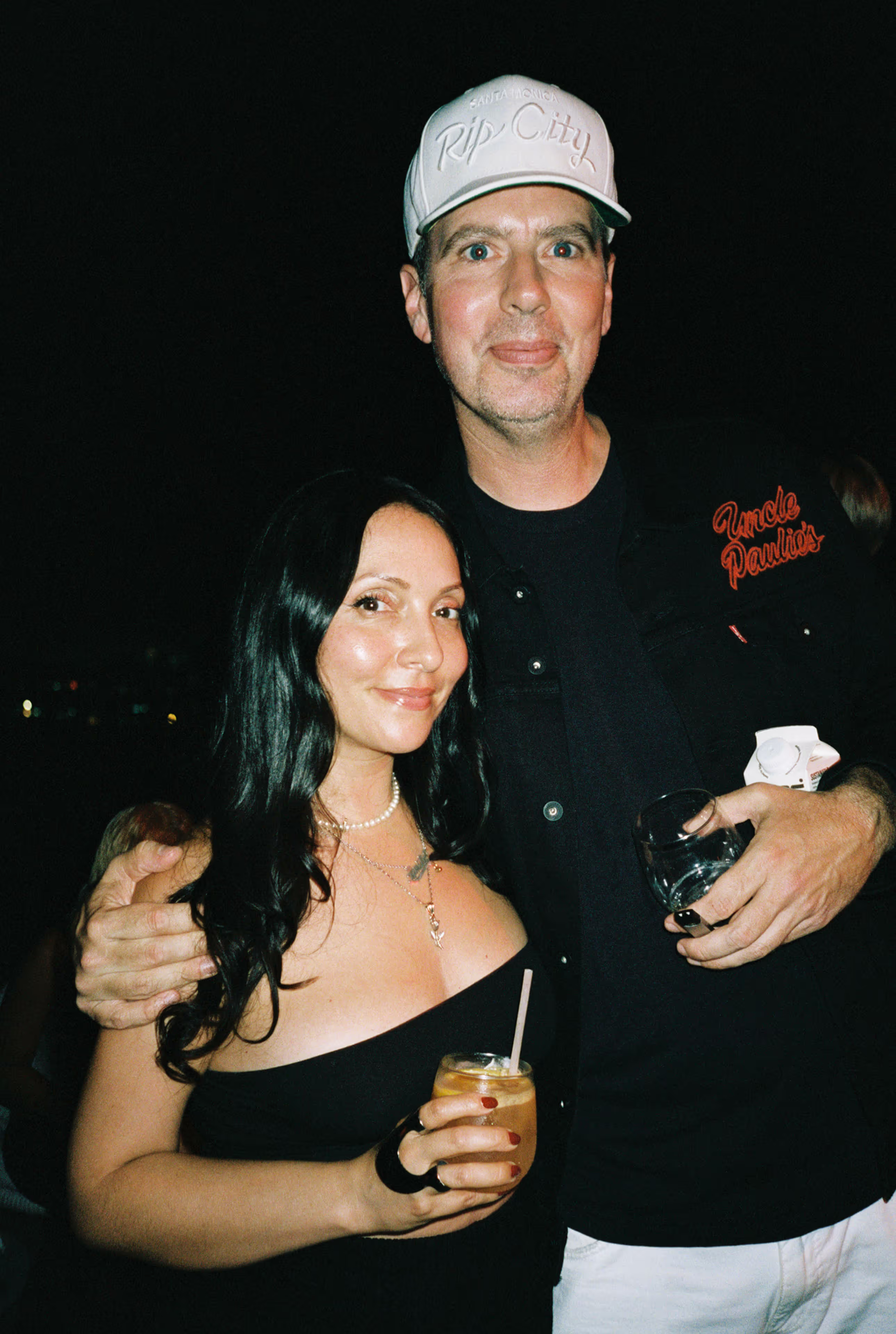 Man wearing a white Rip City cap with arm around a woman in a black strapless dress holding a drink.