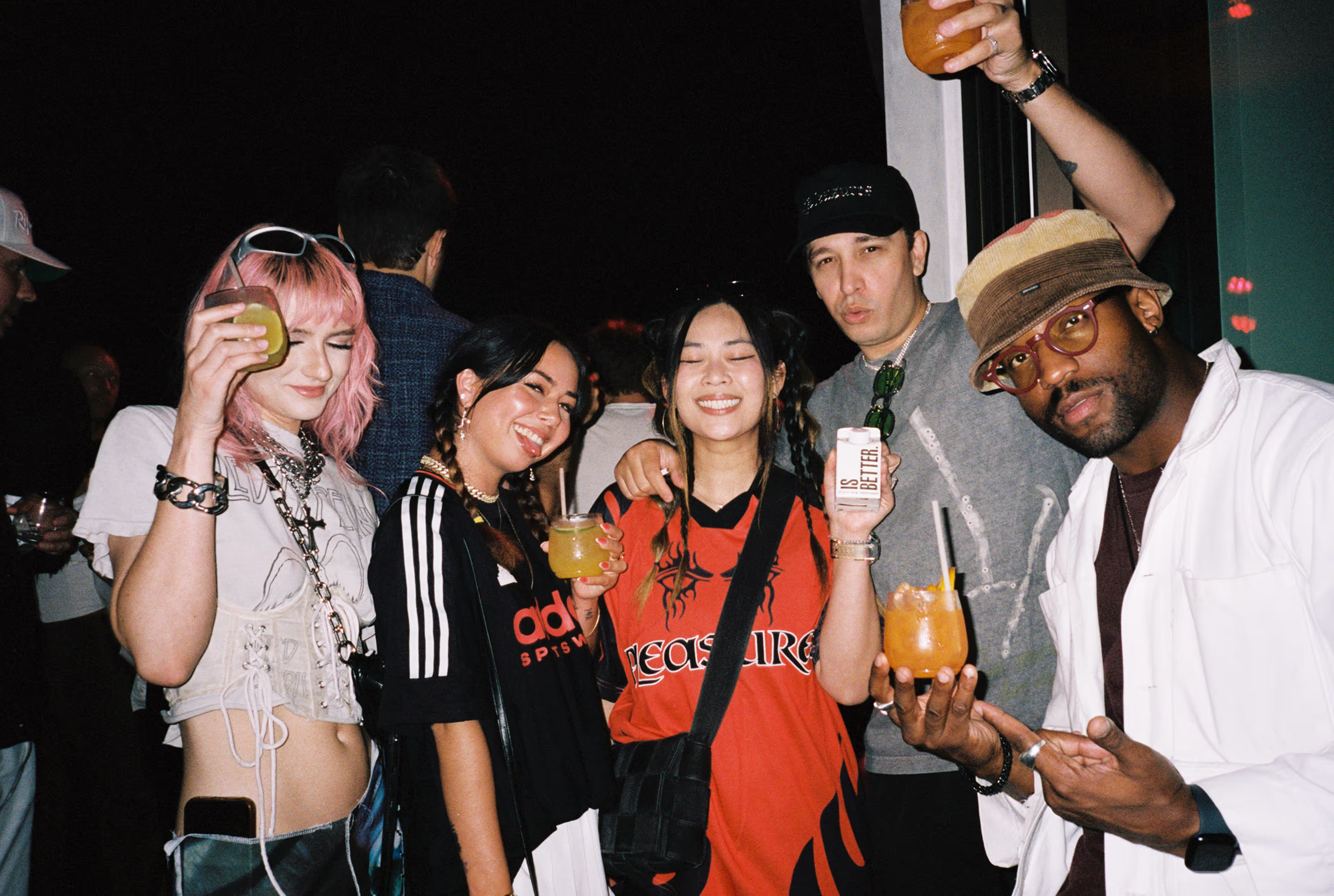 Five young adults posing together at a party, smiling and holding colorful drinks.