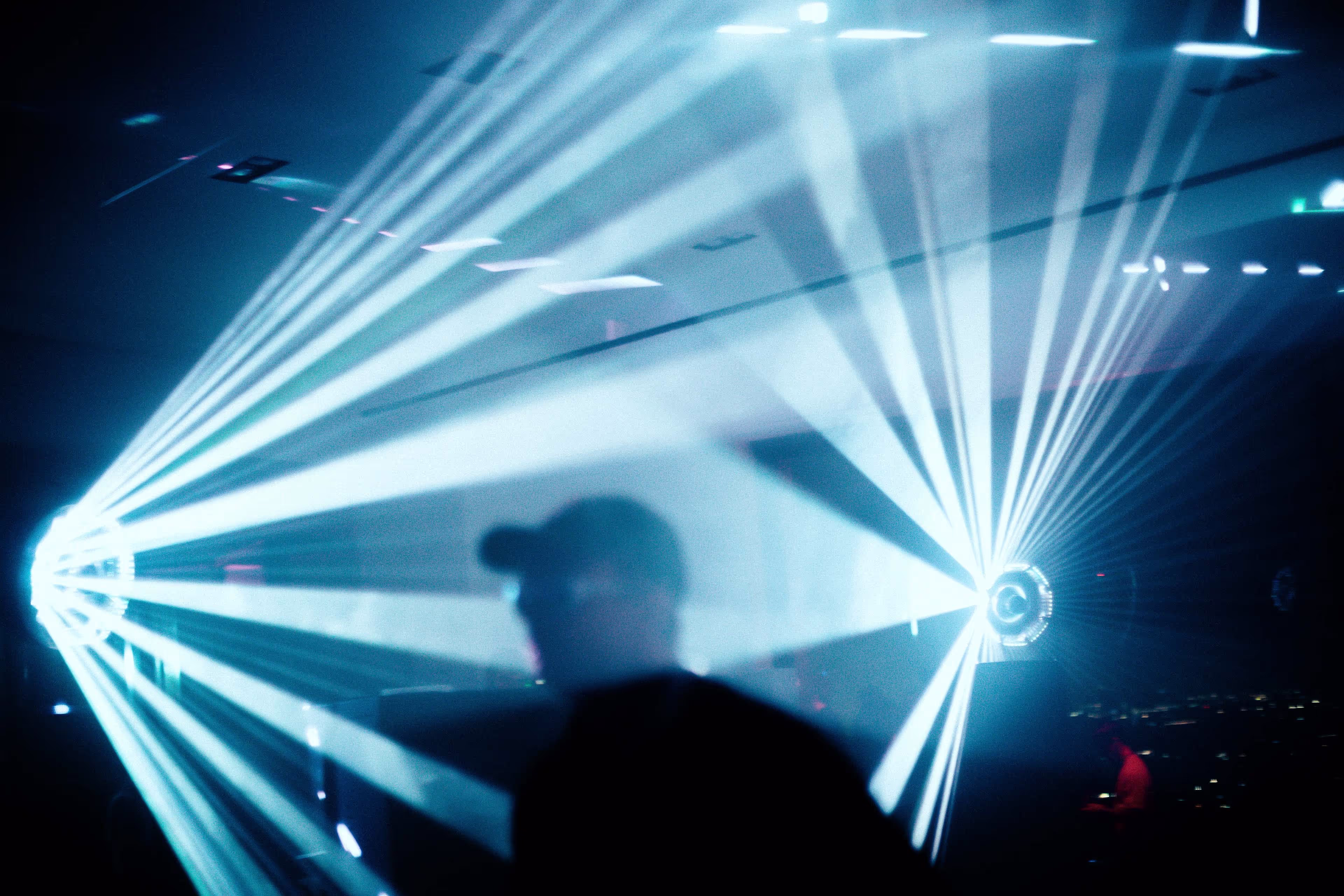 Silhouetted person in a dark room with bright white beams of light radiating from two light sources on opposite sides.