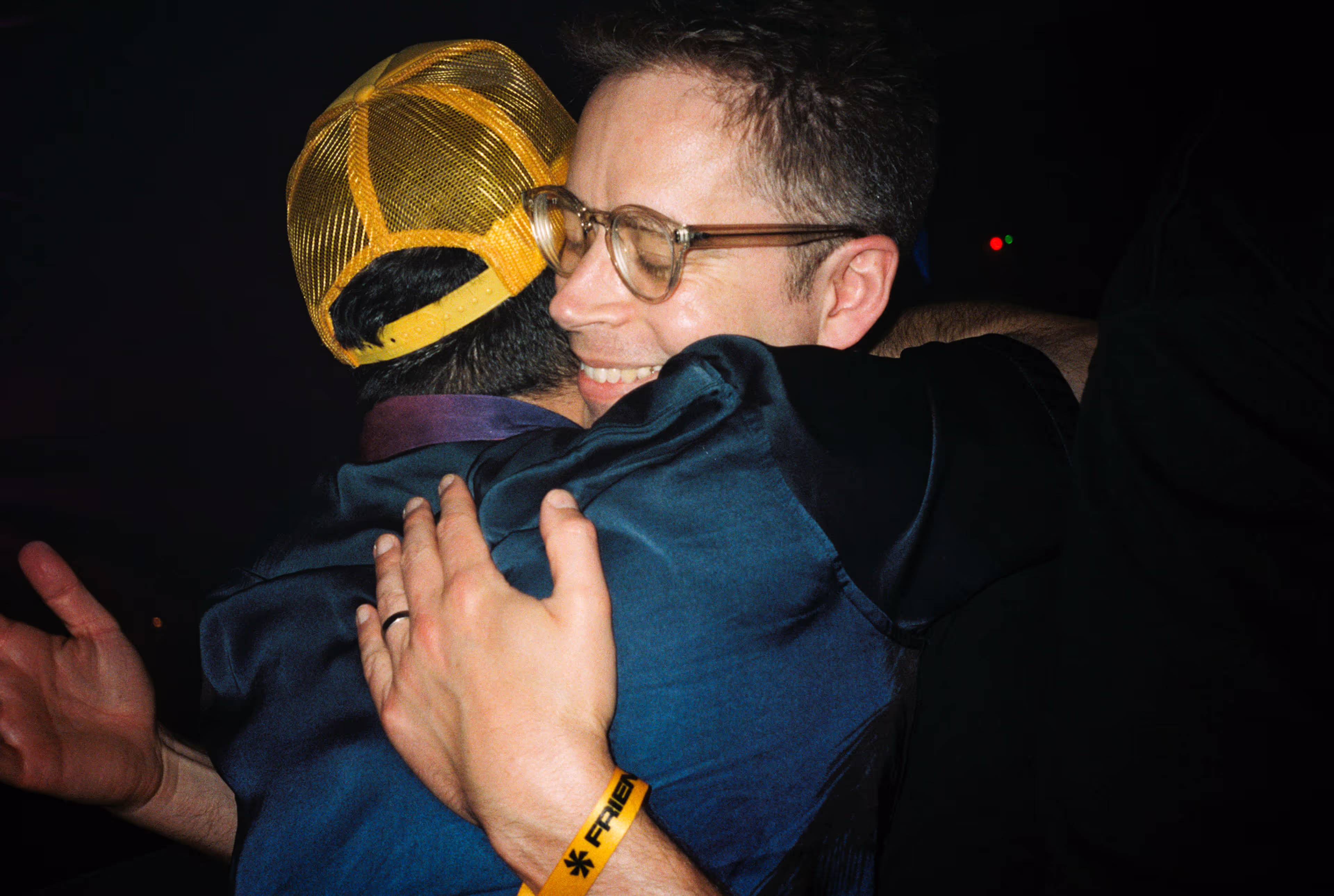 Two men warmly embracing, one wearing a yellow mesh cap.