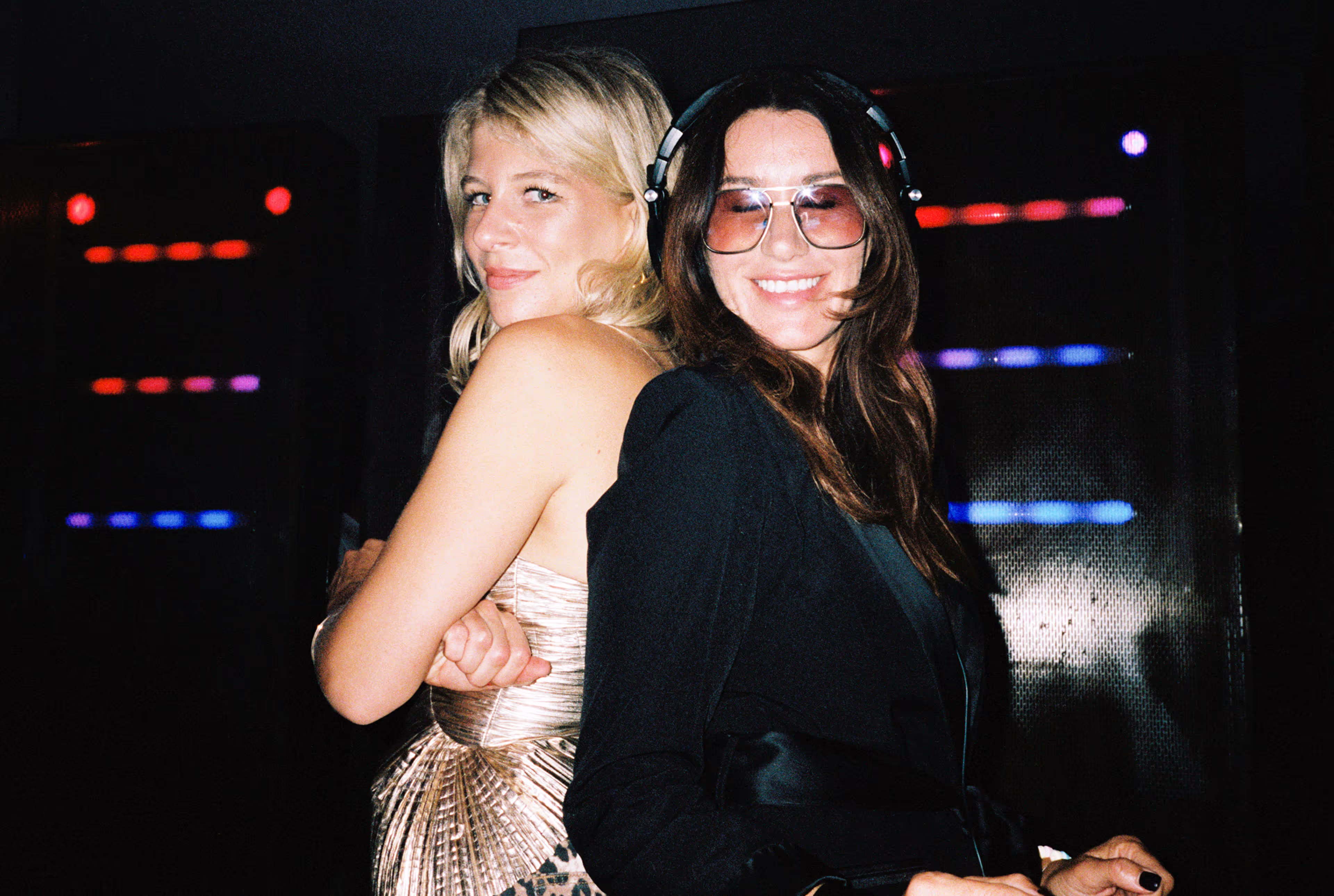 Two women standing back to back at a party.