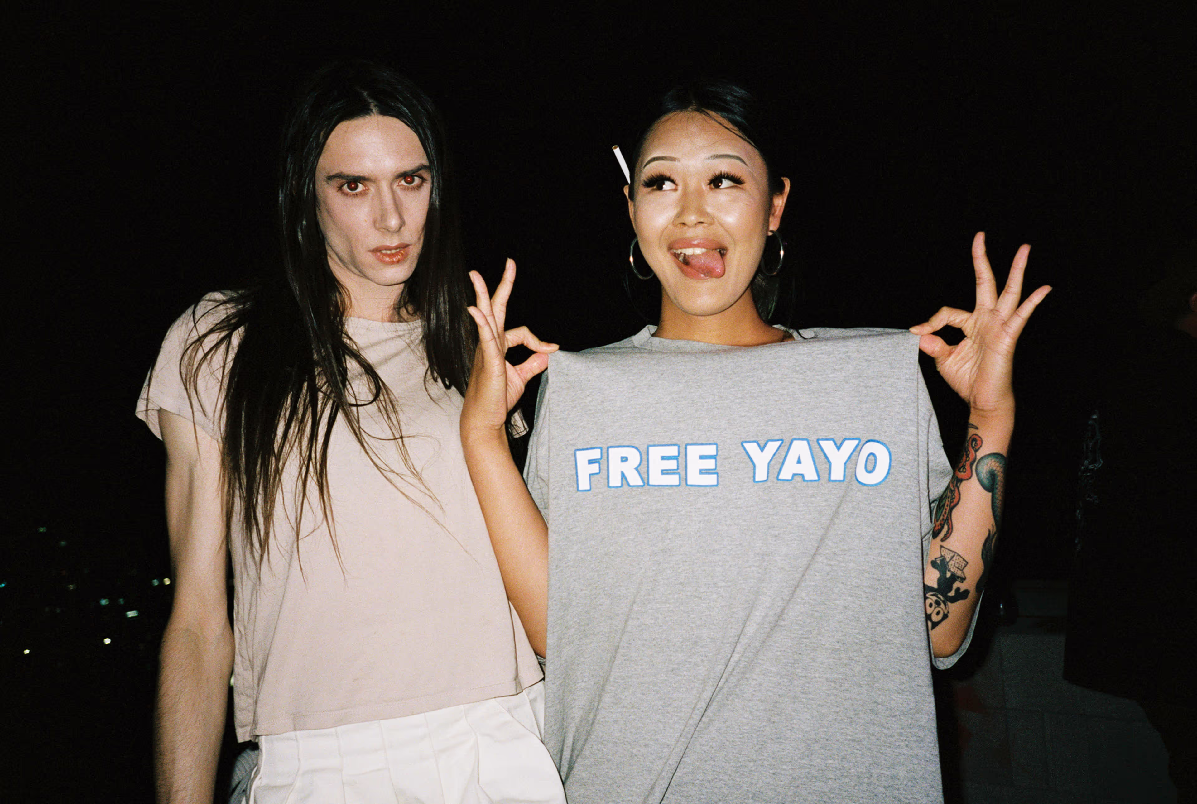 Two people in front of a dark background with one holding a printed shirt.