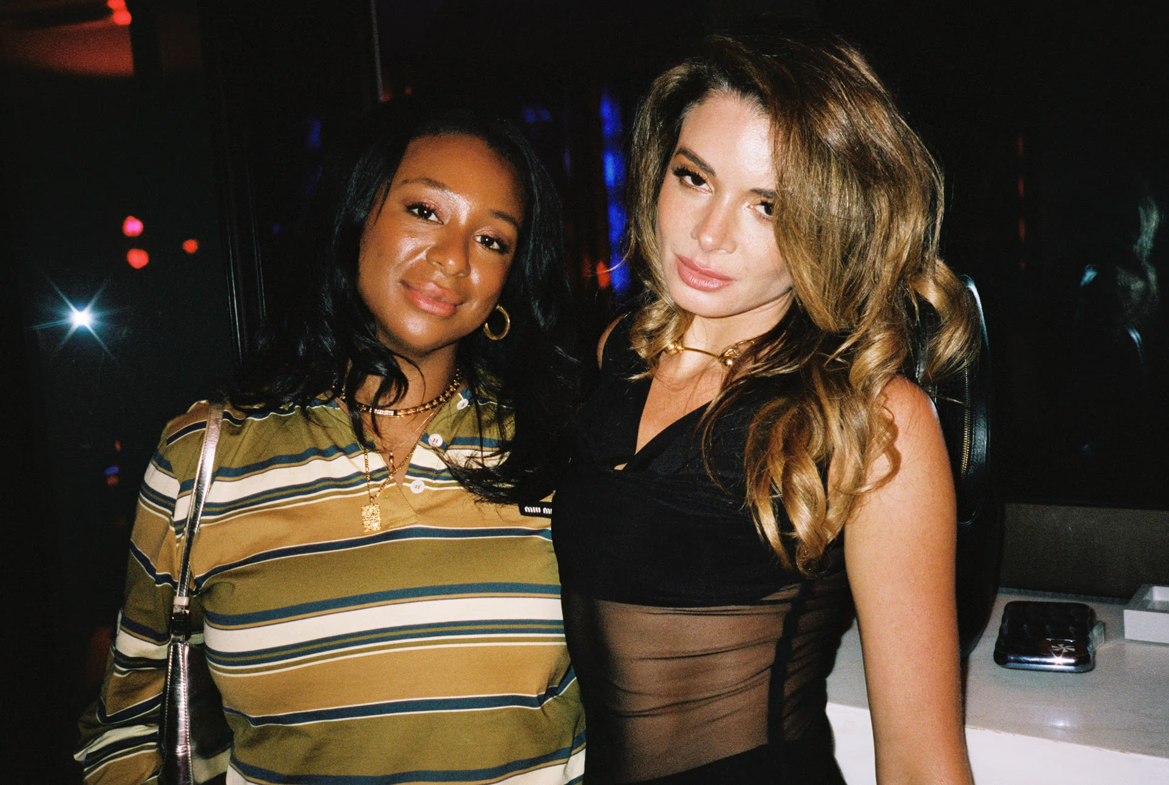 Two women posing together in a dimly lit setting.