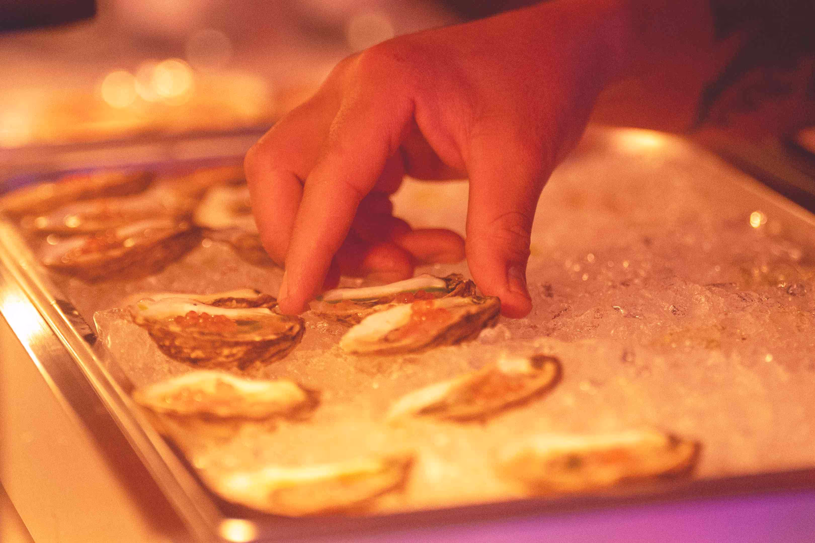 A close up of a person touching a tray of oysters.